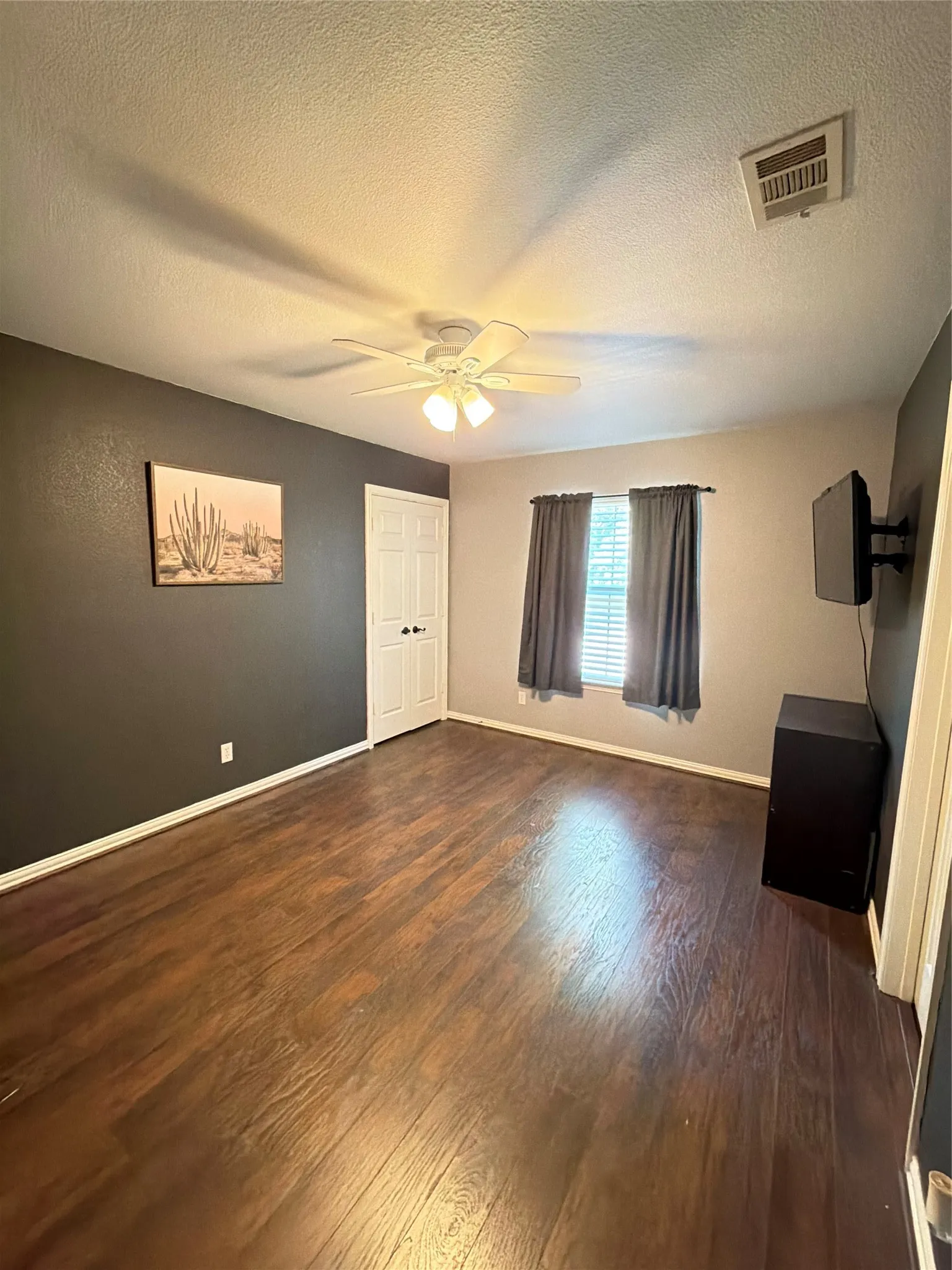 Upstairs bedroom 2. Dark wood-finish flooring, ceiling fan with integrated lighting, window with blinds, and contrasting accent wall