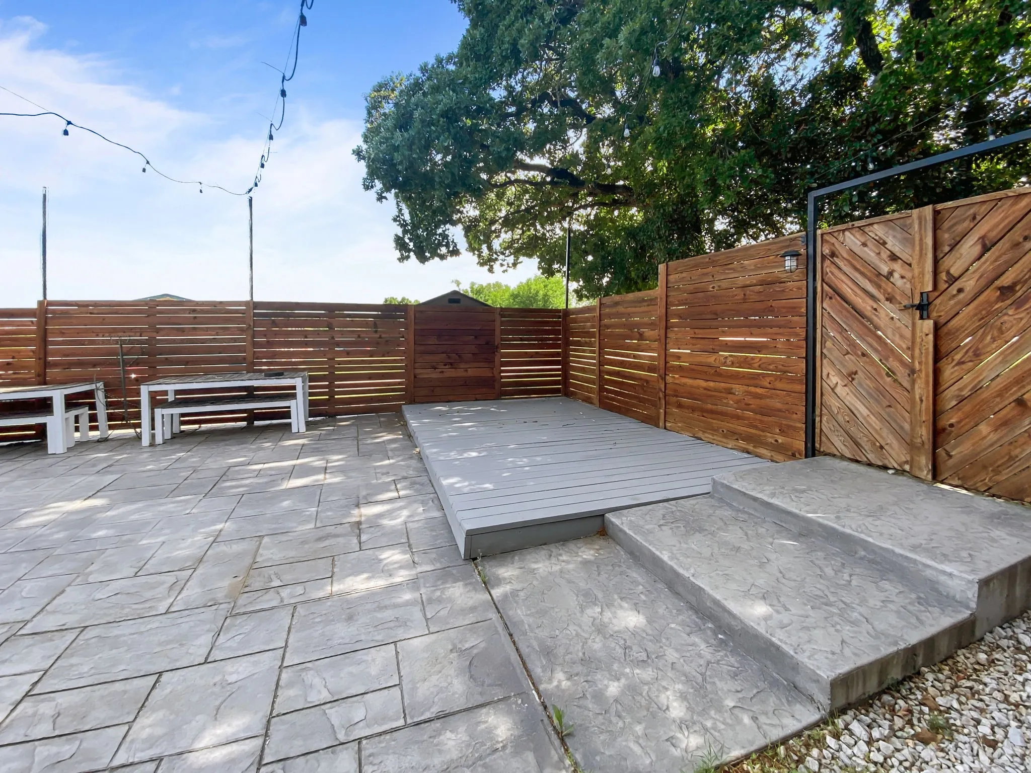 Stamped concrete patio with a raised composite deck, private wood fencing, and a wood gate with metal frame