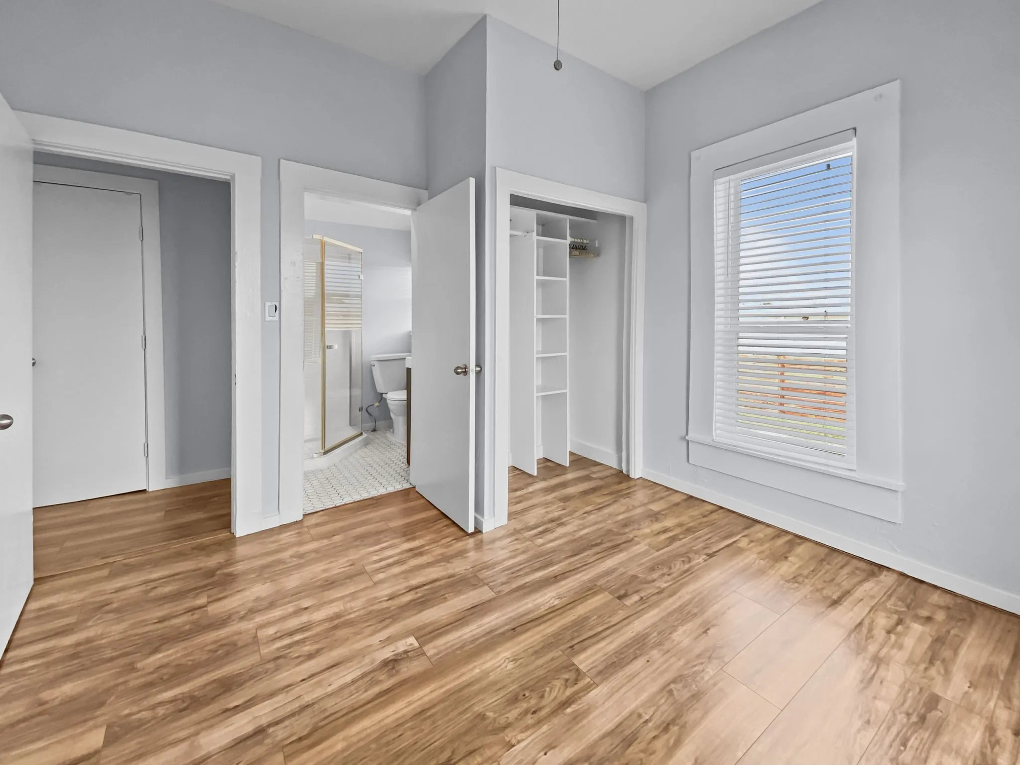 Wood-finish flooring throughout, light blue wall paint, white trim, and a window with blinds