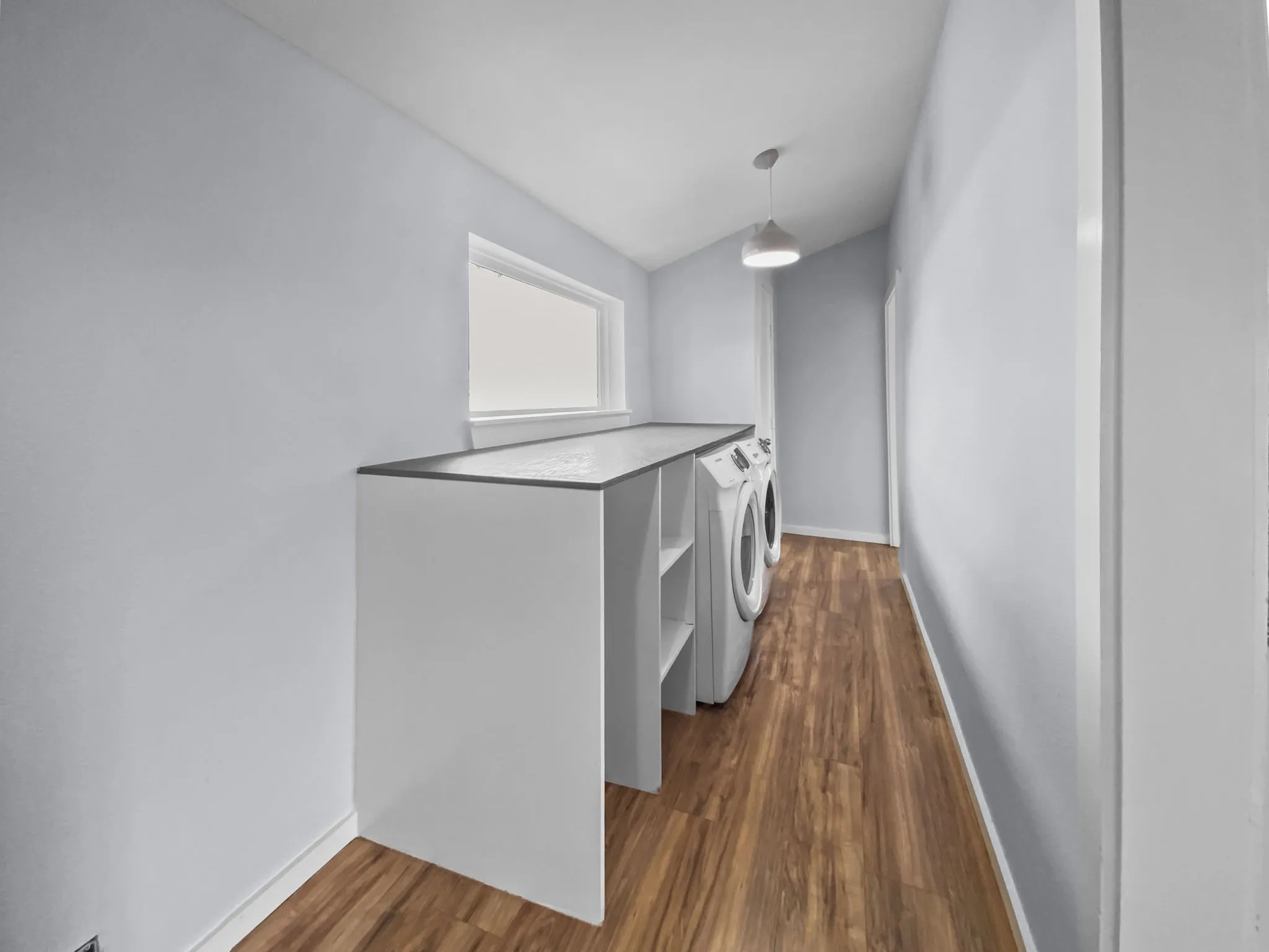 Laundry room featuring wood-finish flooring, a built-in countertop, a window, and a pendant light fixture