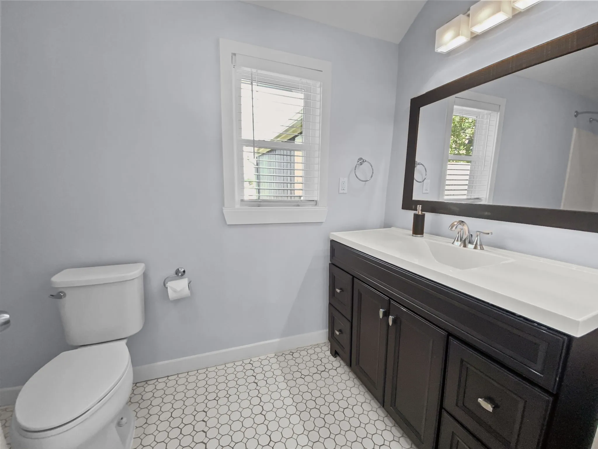 Hexagonal tile flooring, dark wood-finish vanity with white countertop, chrome faucet, and a large framed mirror
