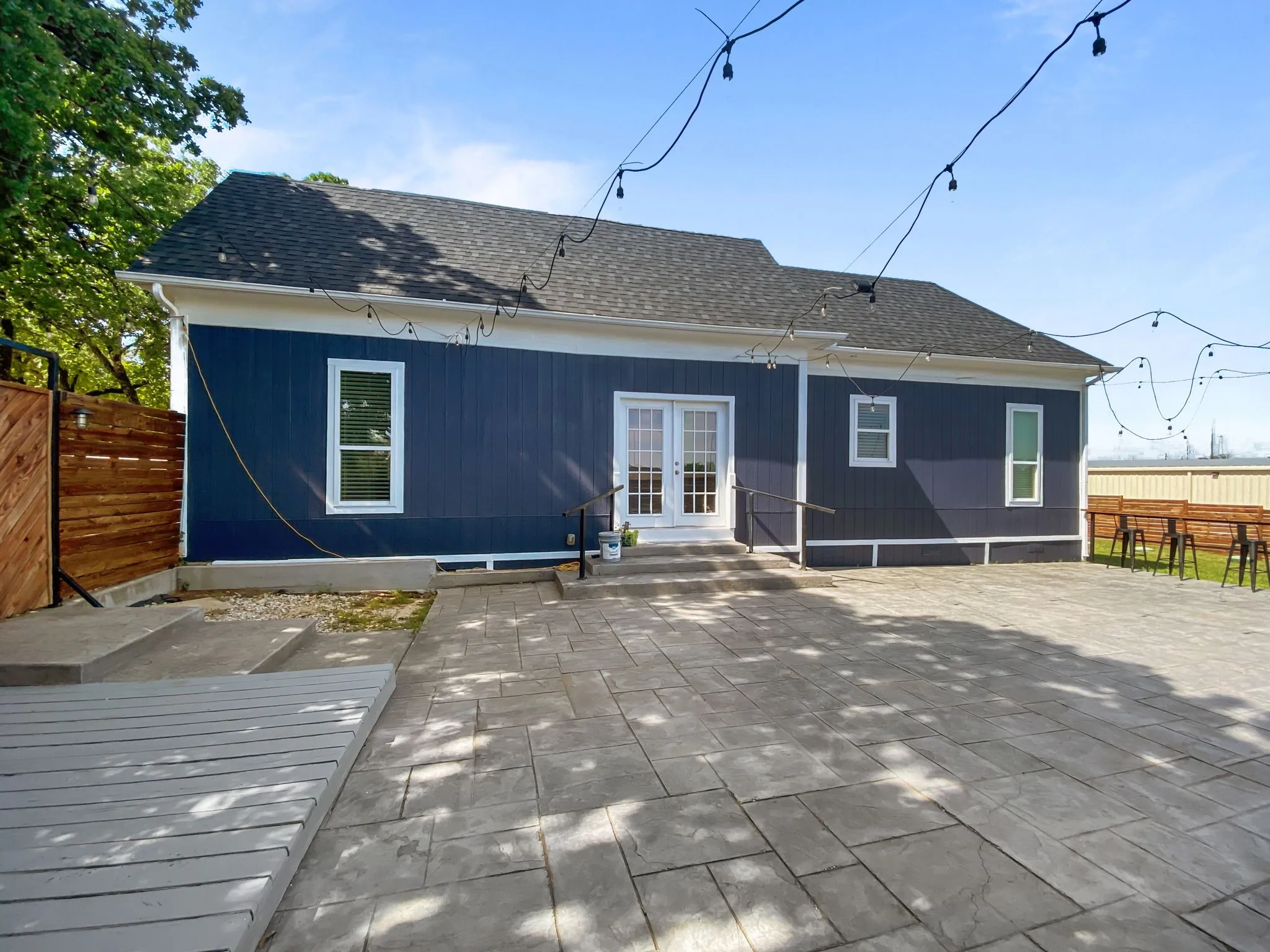 Expansive stamped concrete patio with multiple access points to the structure, featuring French doors and a wood-finish fence