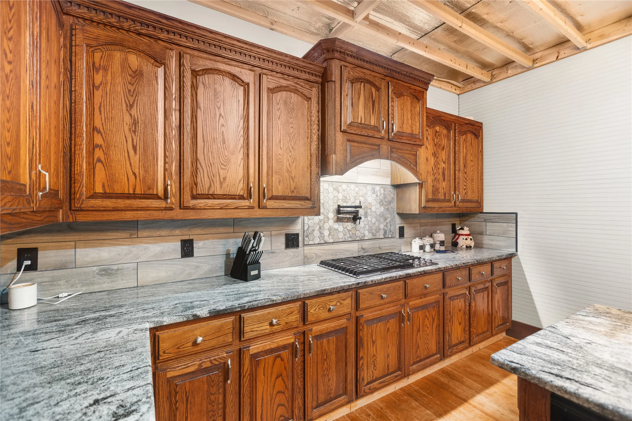 Oak cabinetry with decorative trim, granite countertops, integrated gas cooktop, tile backsplash, and wood flooring