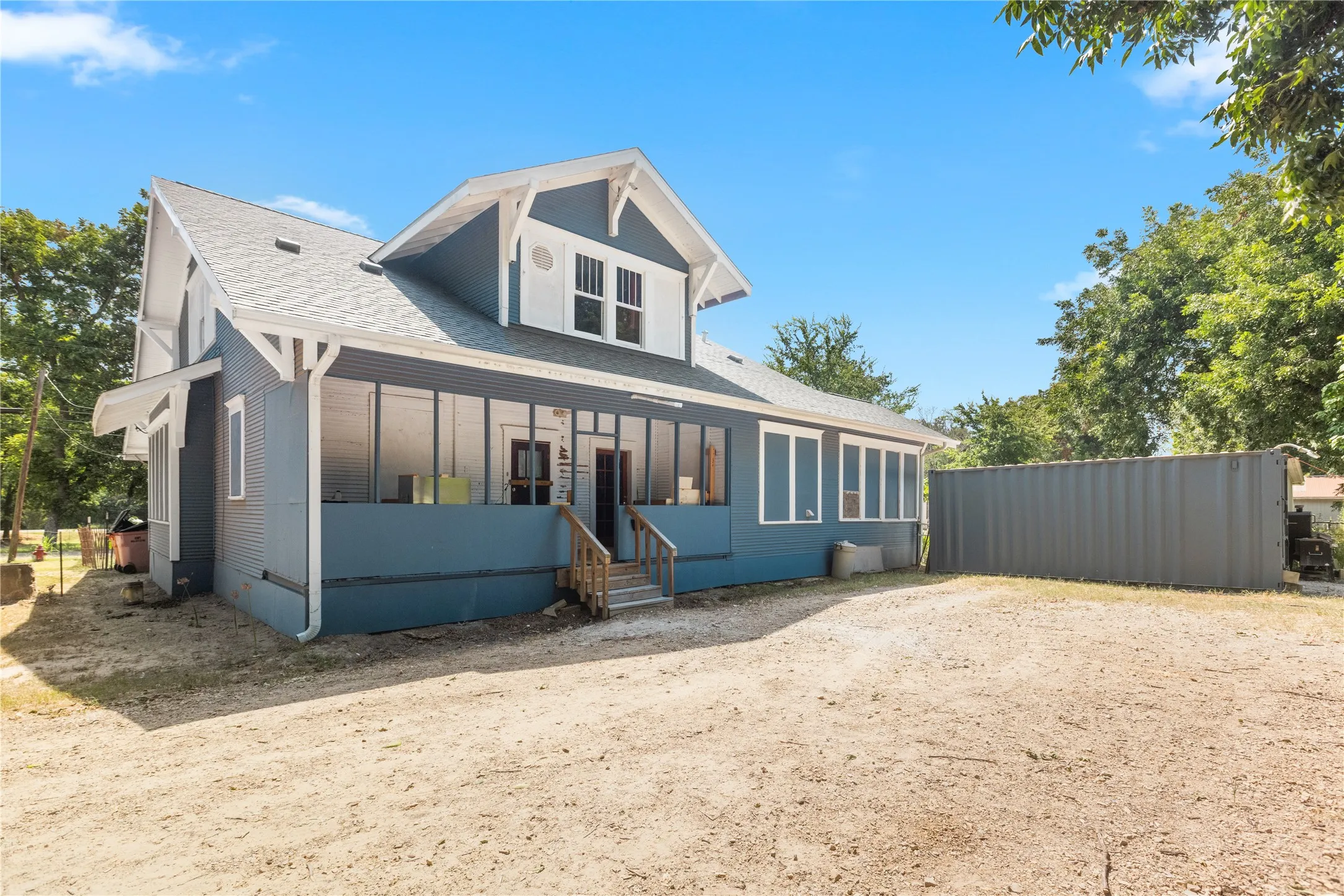 Blue exterior siding with white trim, covered front porch, multi-pane windows, and a peaked roofline