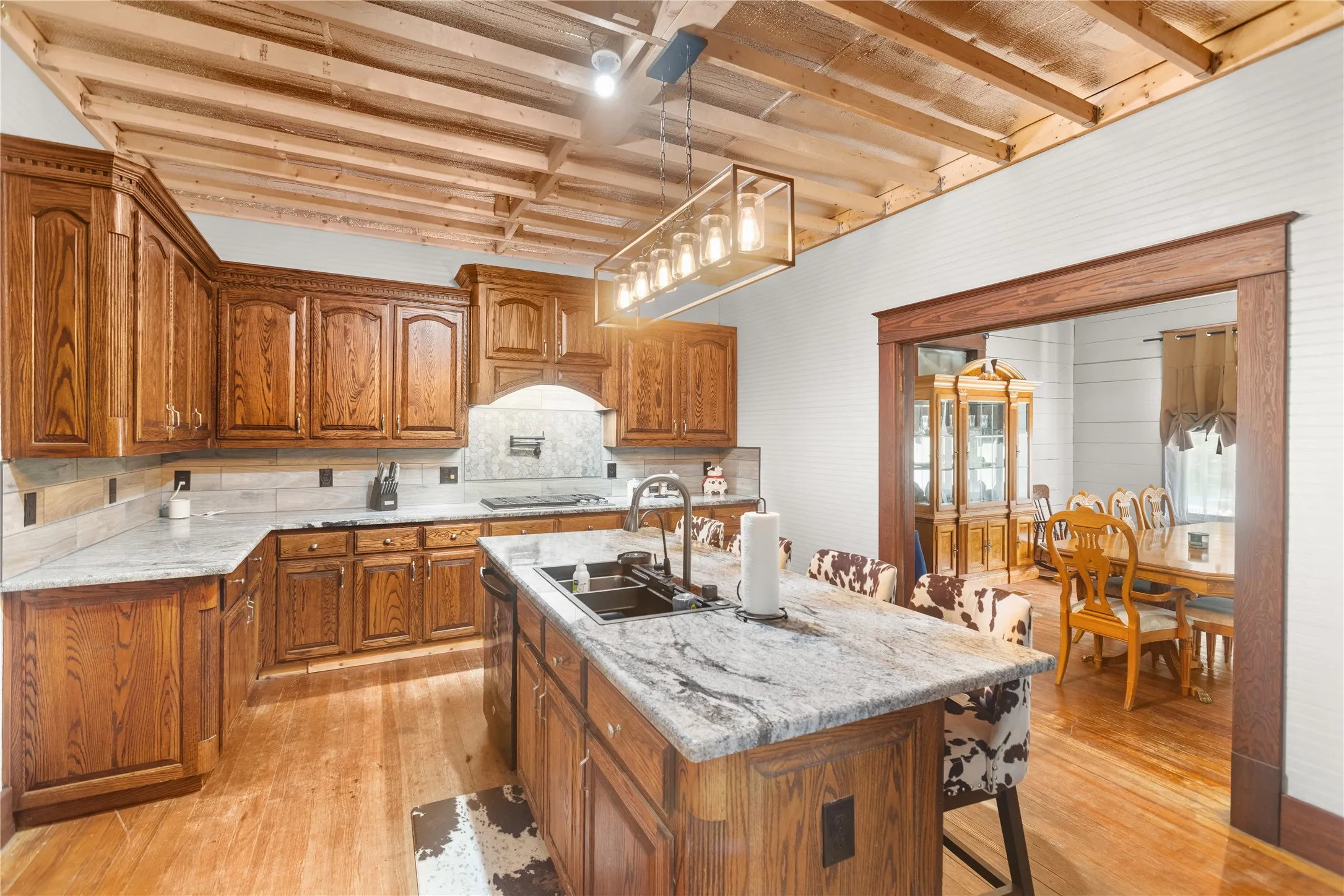 Kitchen featuring wood cabinetry, light-toned wood-finish flooring, a central island with a sink, and a rectangular pendant light fixture