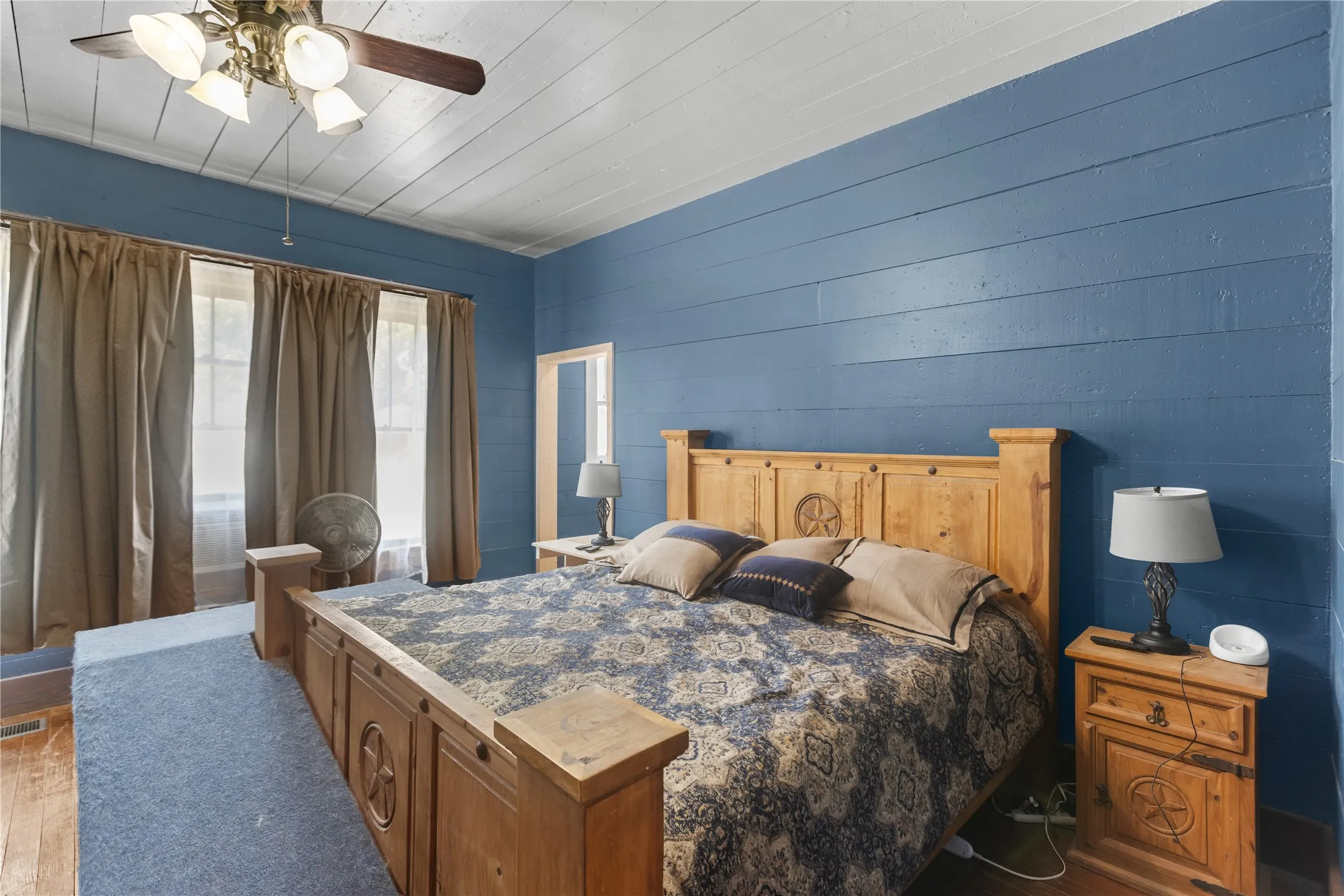 Shiplap accent wall, wood-paneled ceiling, ceiling fan with light fixture, window openings, wood flooring