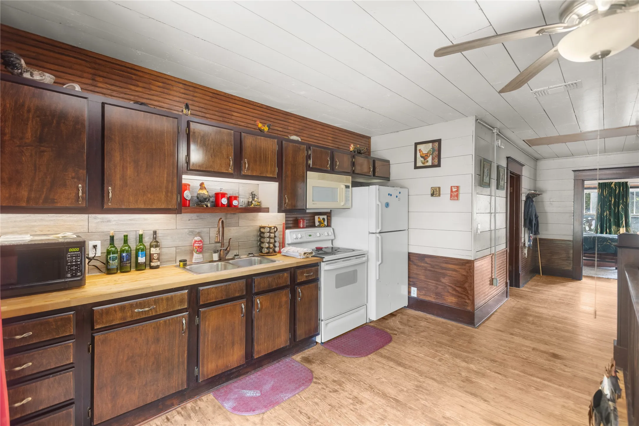 Kitchen featuring wood flooring, dark wood cabinetry, white appliances, a double basin sink, and a ceiling fan