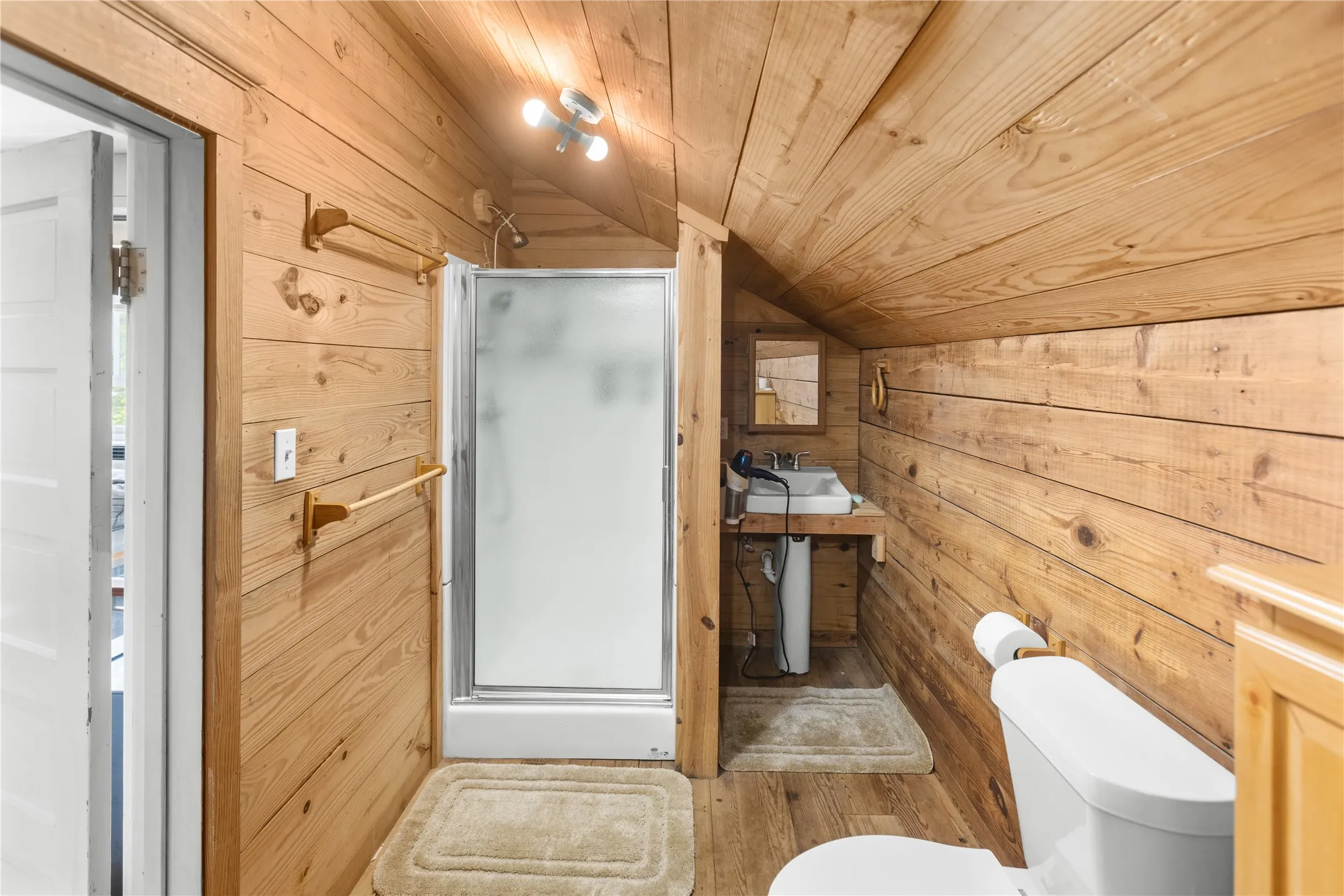 Wood interior featuring a shower enclosure, pedestal sink, and toilet