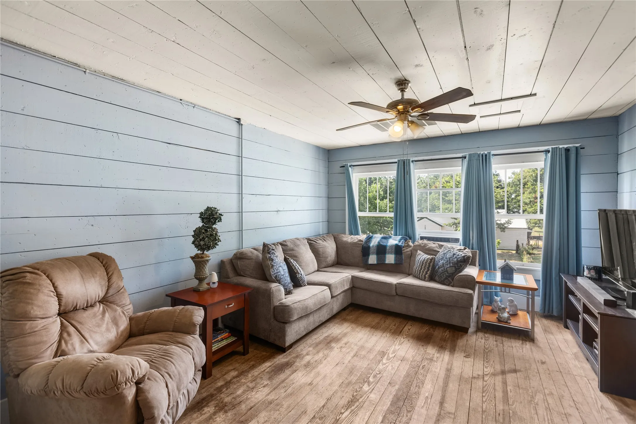 Shiplap wall paneling, wood-finish flooring, white plank ceiling, multiple windows, and a ceiling fan with integrated lighting