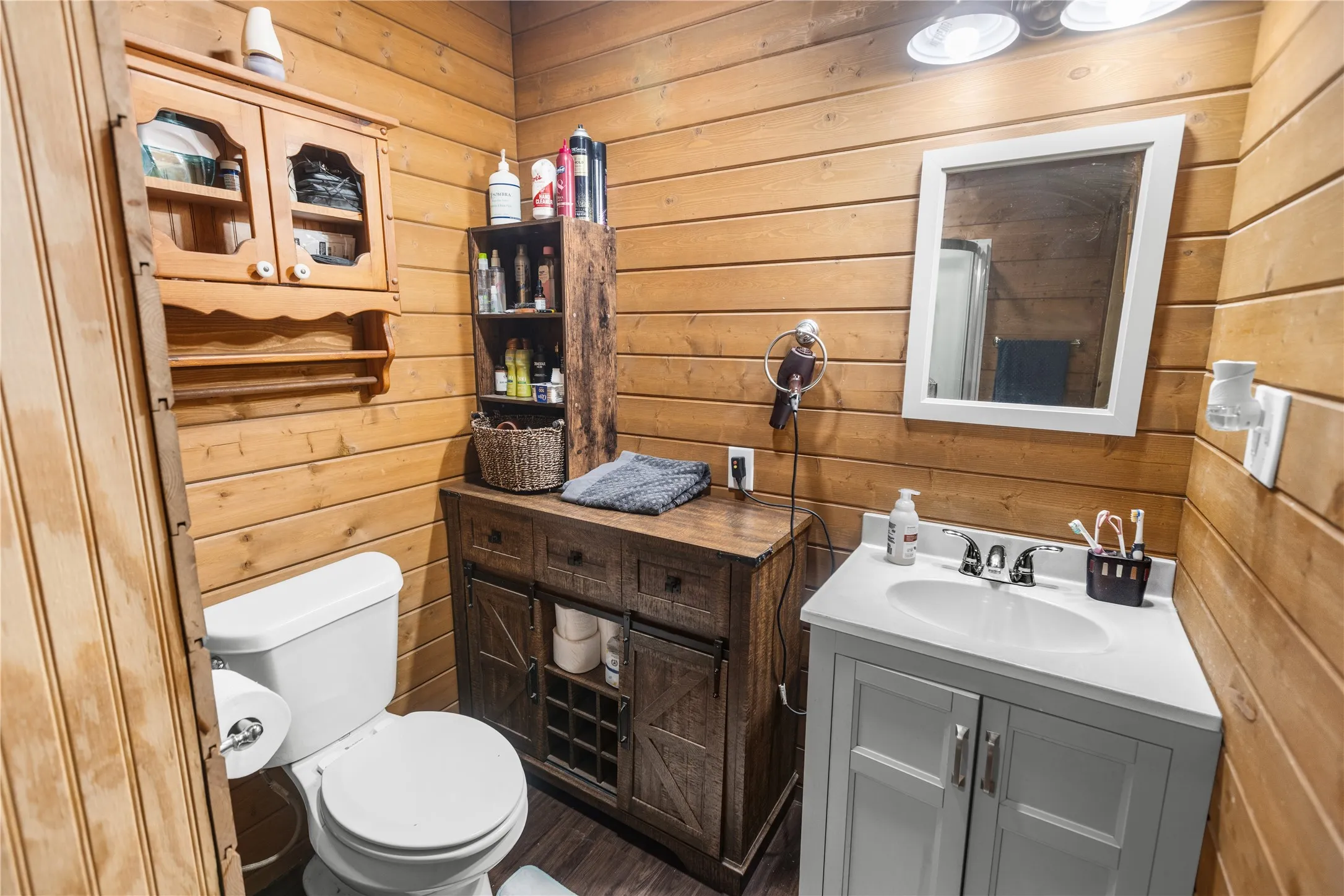 Wood bathroom featuring a white toilet, light gray vanity with an integrated sink, and a framed mirror