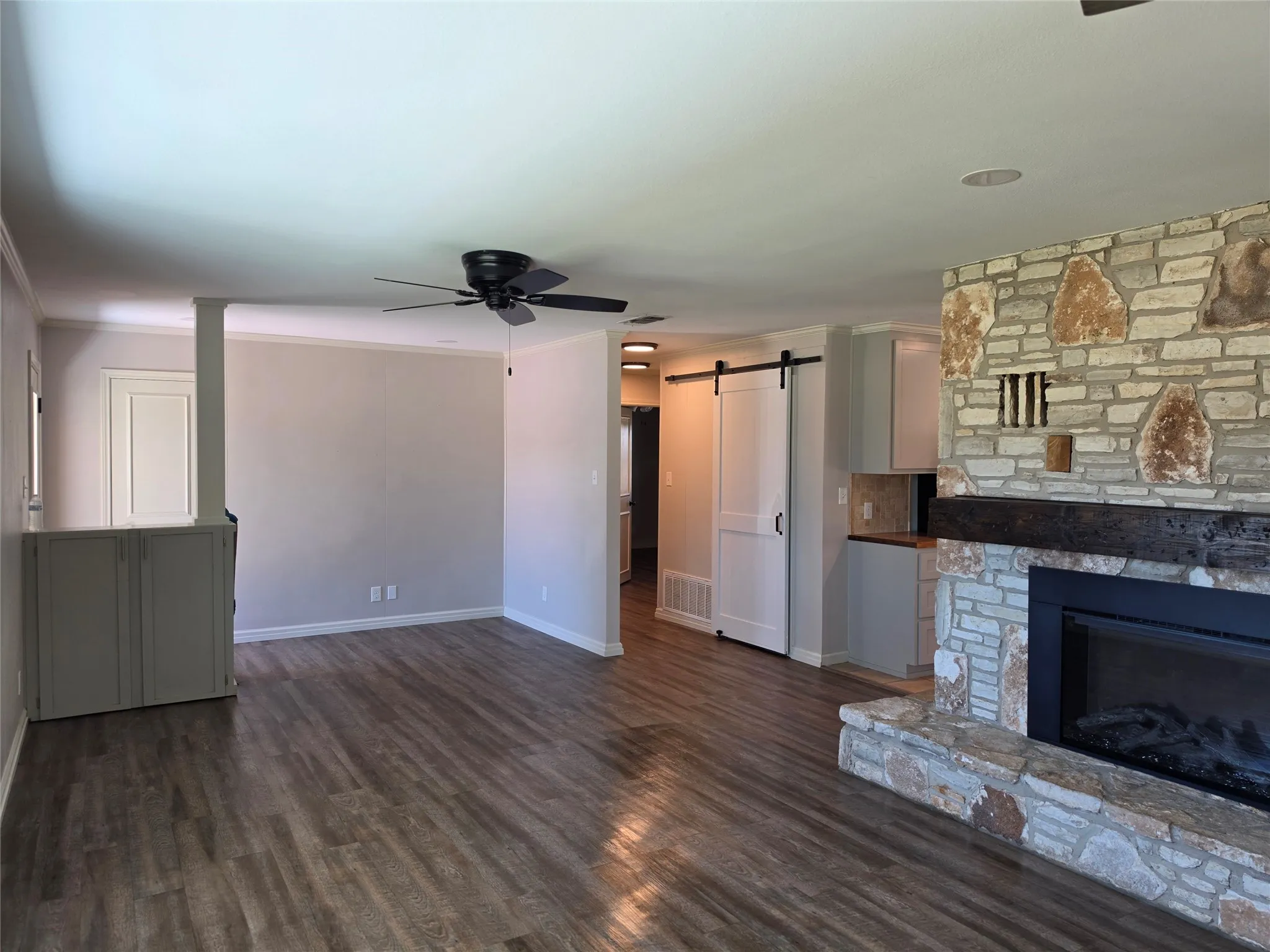Stone-finish fireplace with dark wood mantel, wood-finish flooring, and white barn door