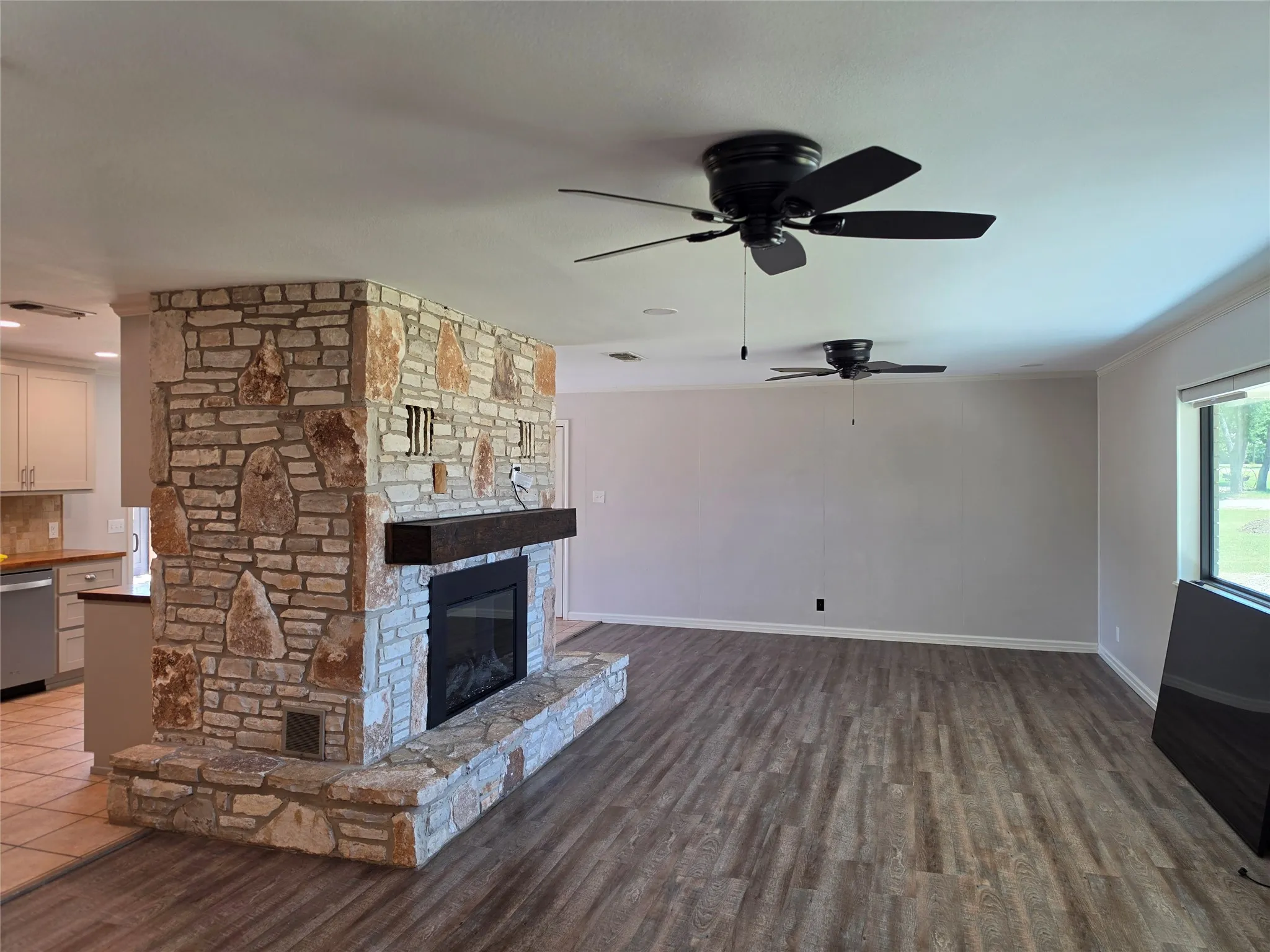 Stone-clad fireplace with hearth, wood-finish flooring, two ceiling fans, and a large window