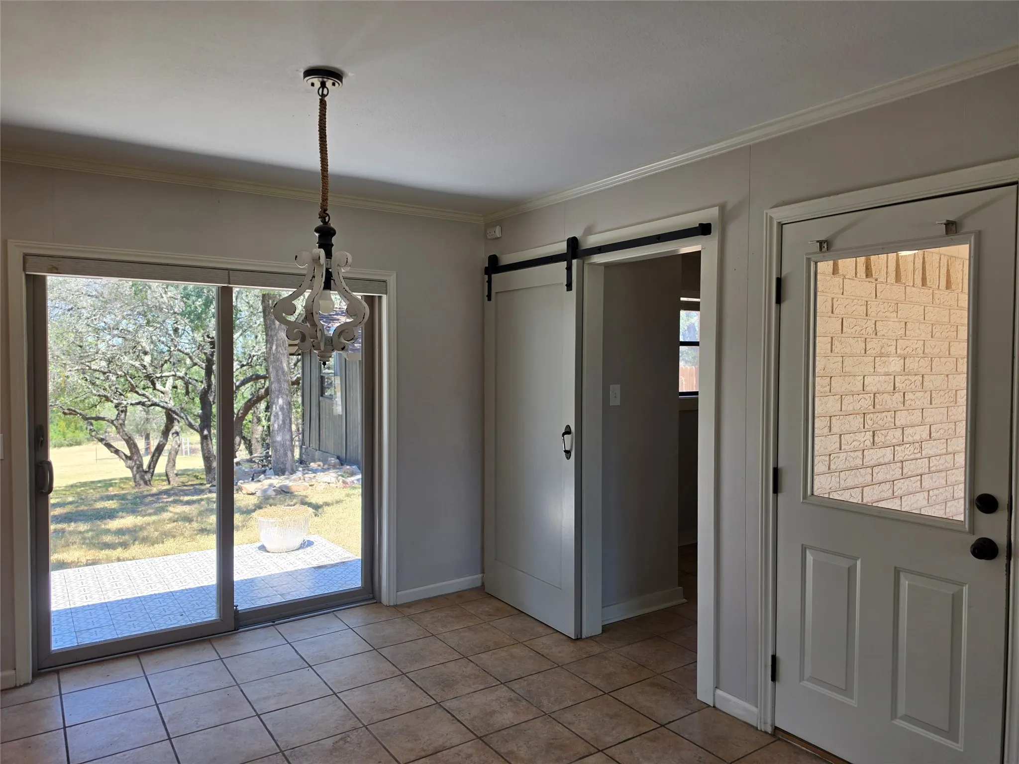 Tile flooring, sliding glass patio door, decorative pendant light, barn door, and exterior brick wall