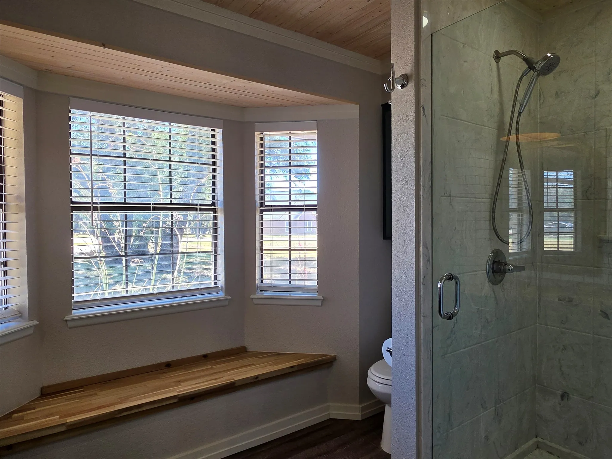 Wood-finish flooring with a glass-enclosed shower, featuring tiled walls and a built-in bench under bay windows
