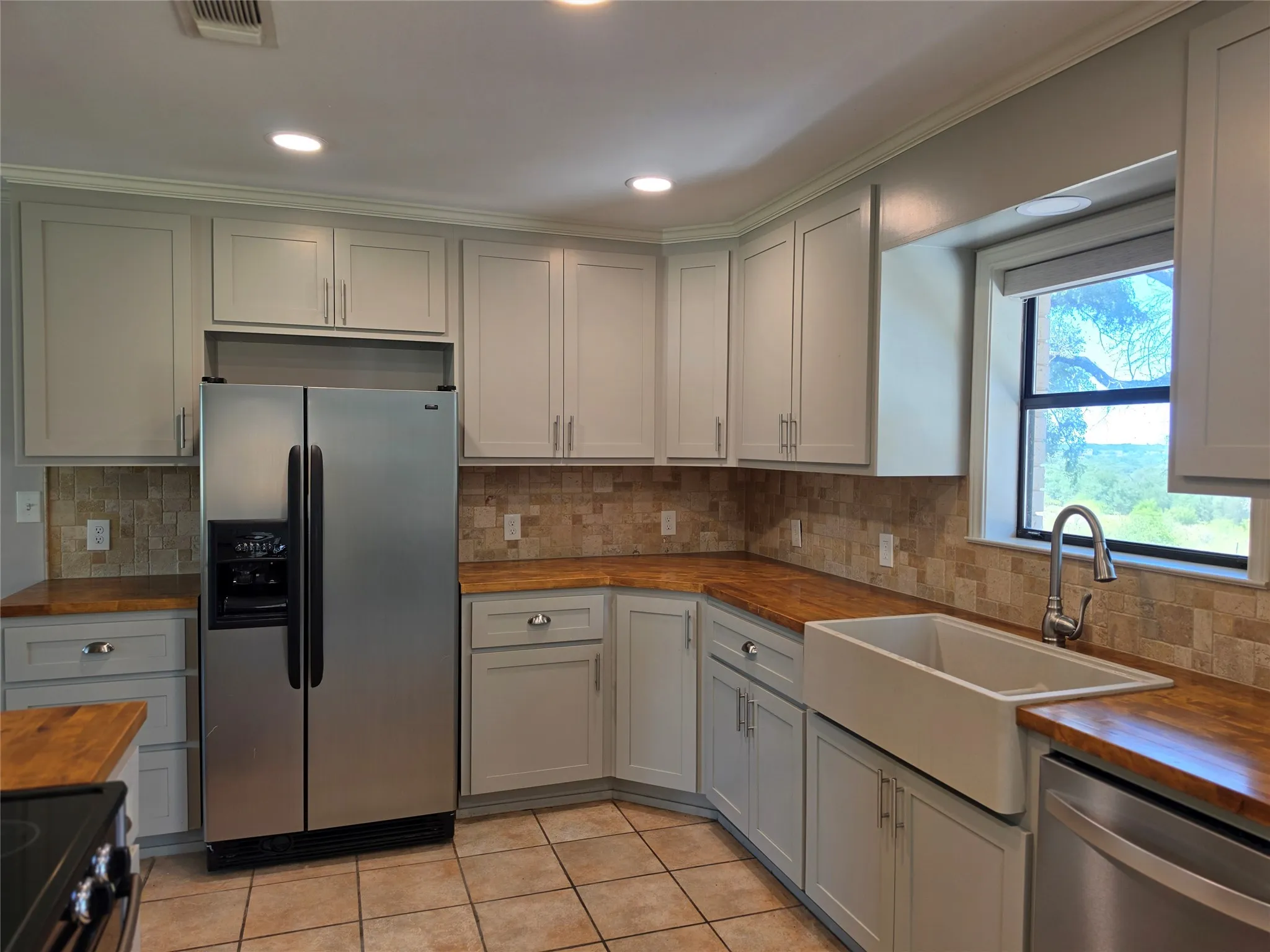 Kitchen featuring light-toned cabinetry, wood-finish countertops, and a full-height tile backsplash