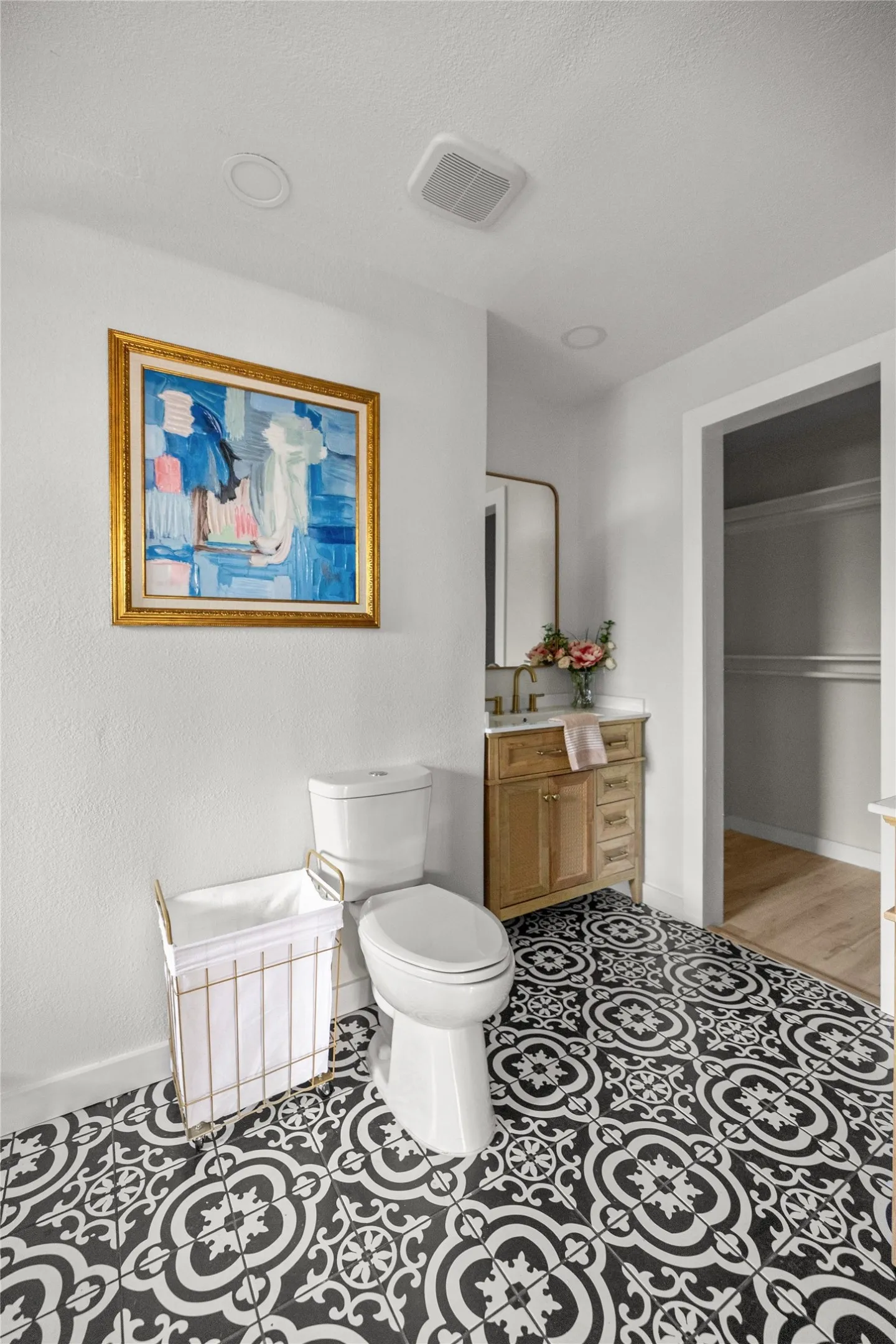 Decorative floor tile, white toilet, single vanity with wood-finish cabinetry, countertop, and a wall-mounted mirror