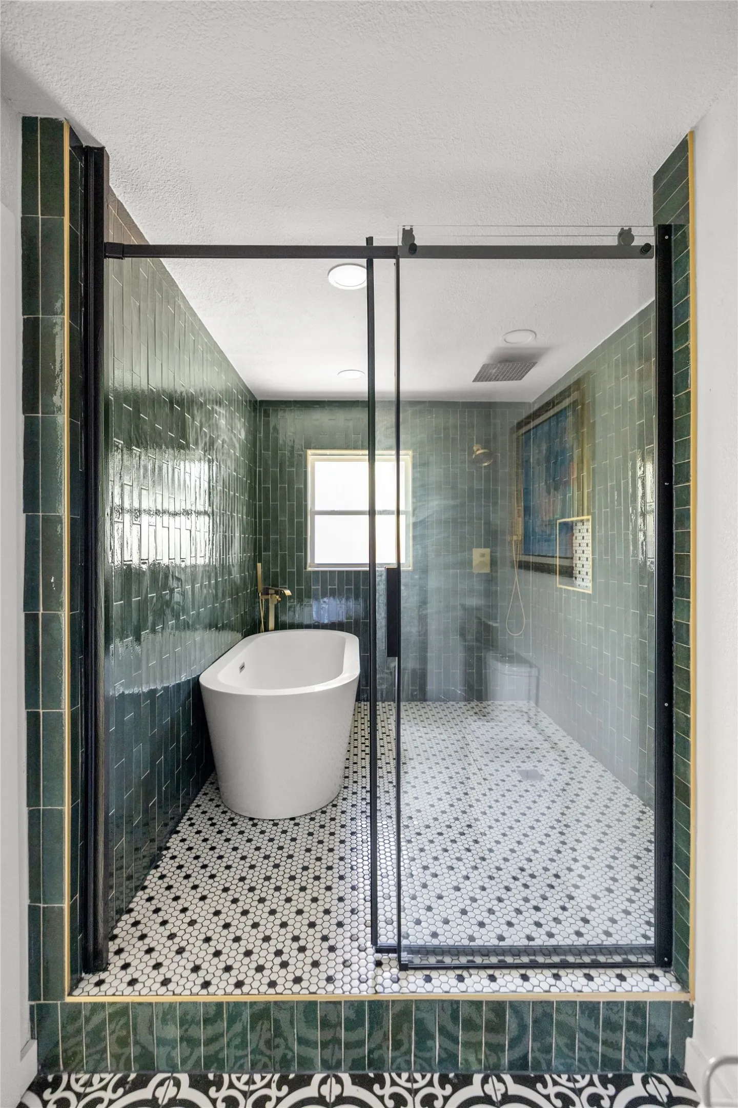 Freestanding soaking tub, glass-enclosed walk-in shower, green subway tile walls, black and white hexagonal floor tiling, and a window for natural light