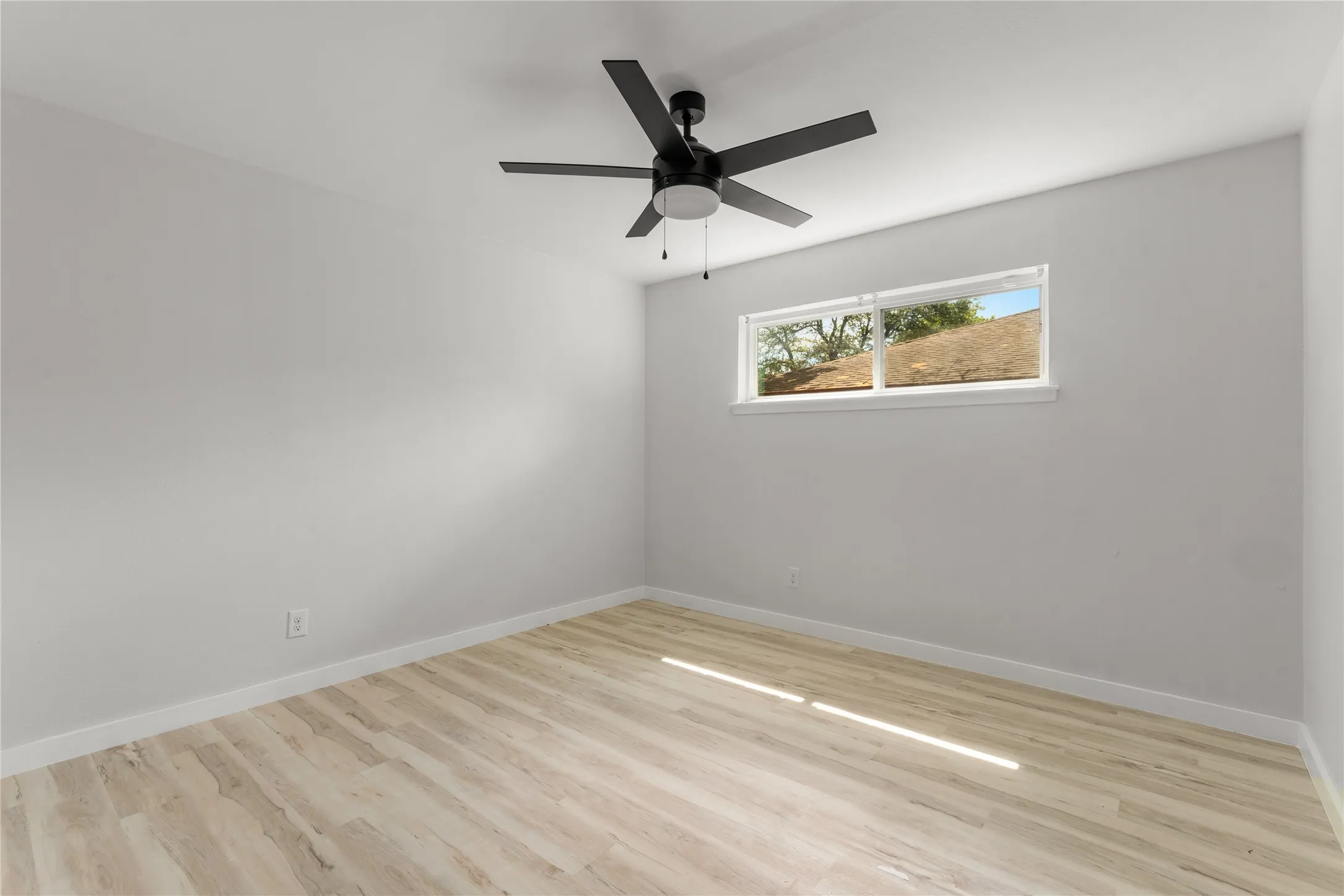 Wood-finish flooring, white walls, and a black ceiling fan with an integrated light