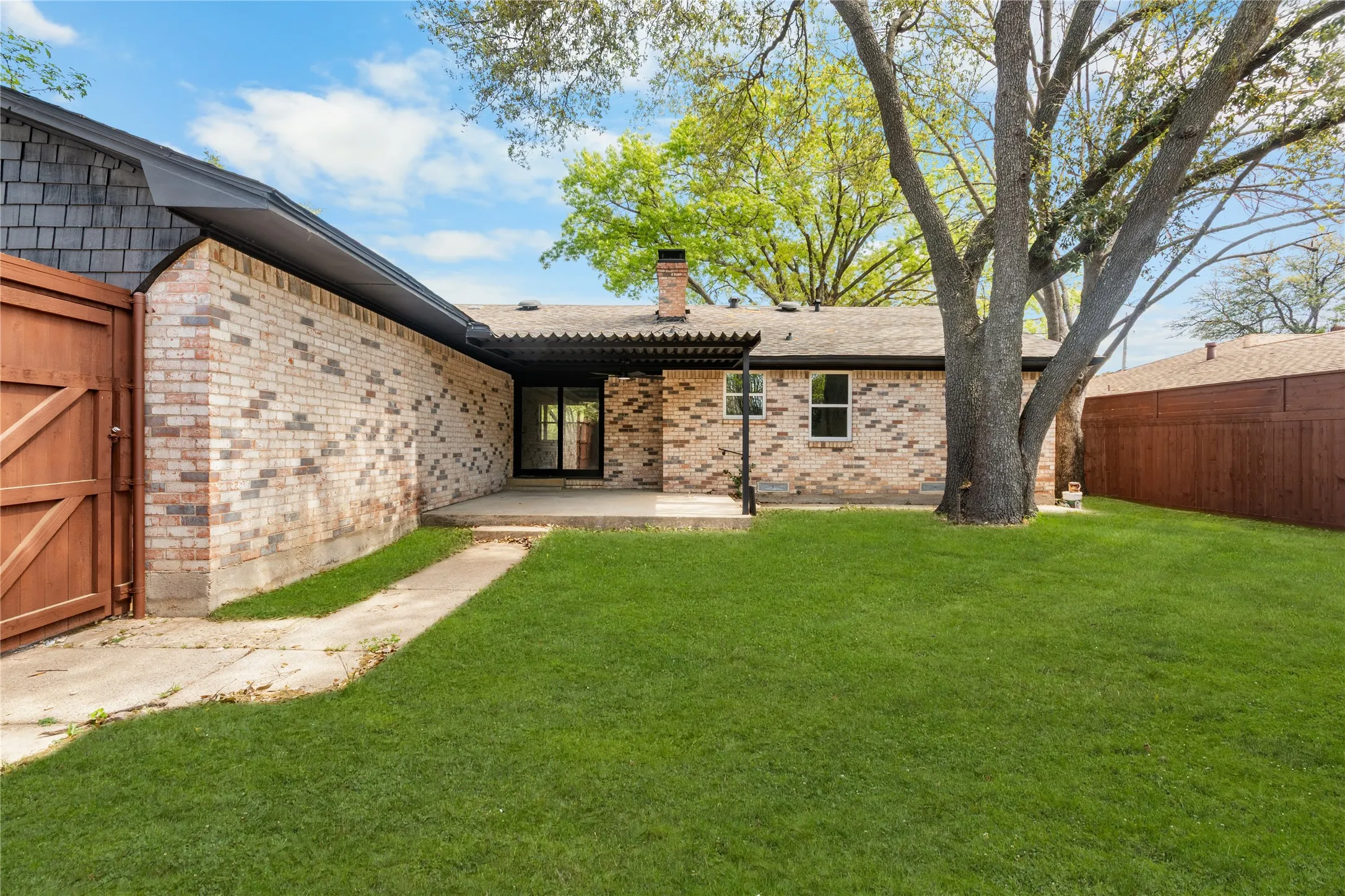 Expansive backyard featuring a manicured lawn, mature trees, and a concrete patio