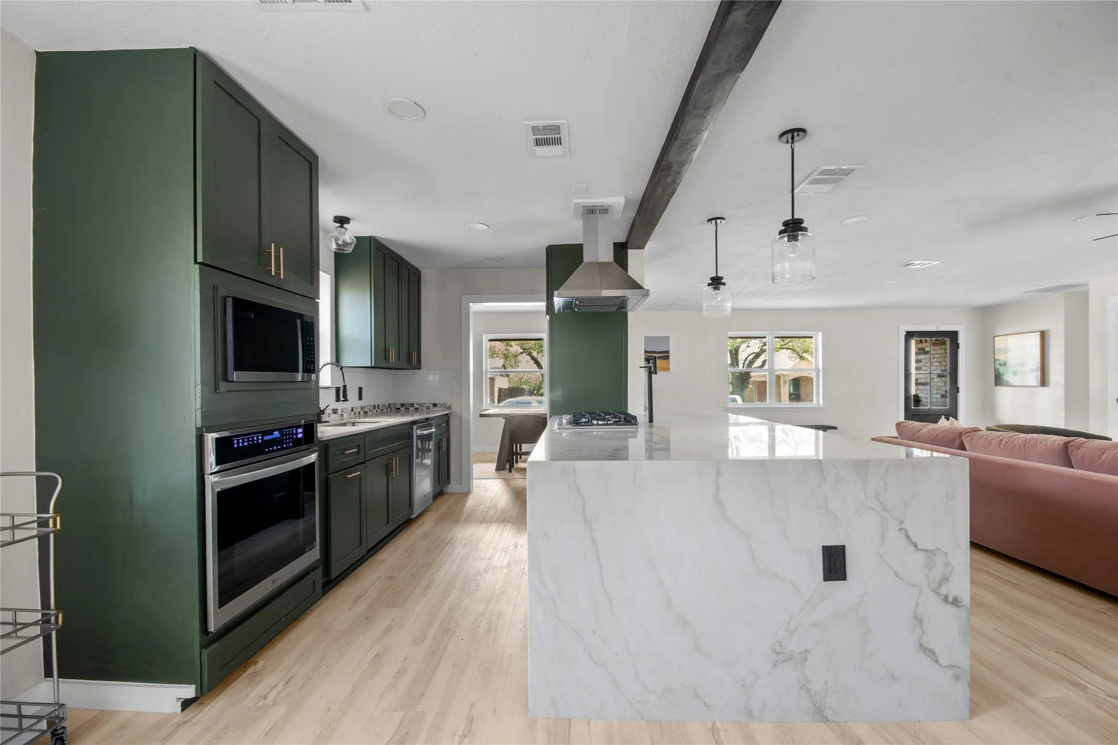 Kitchen featuring dark green cabinetry, stainless steel appliances, a white stone island, and wood-finish flooring