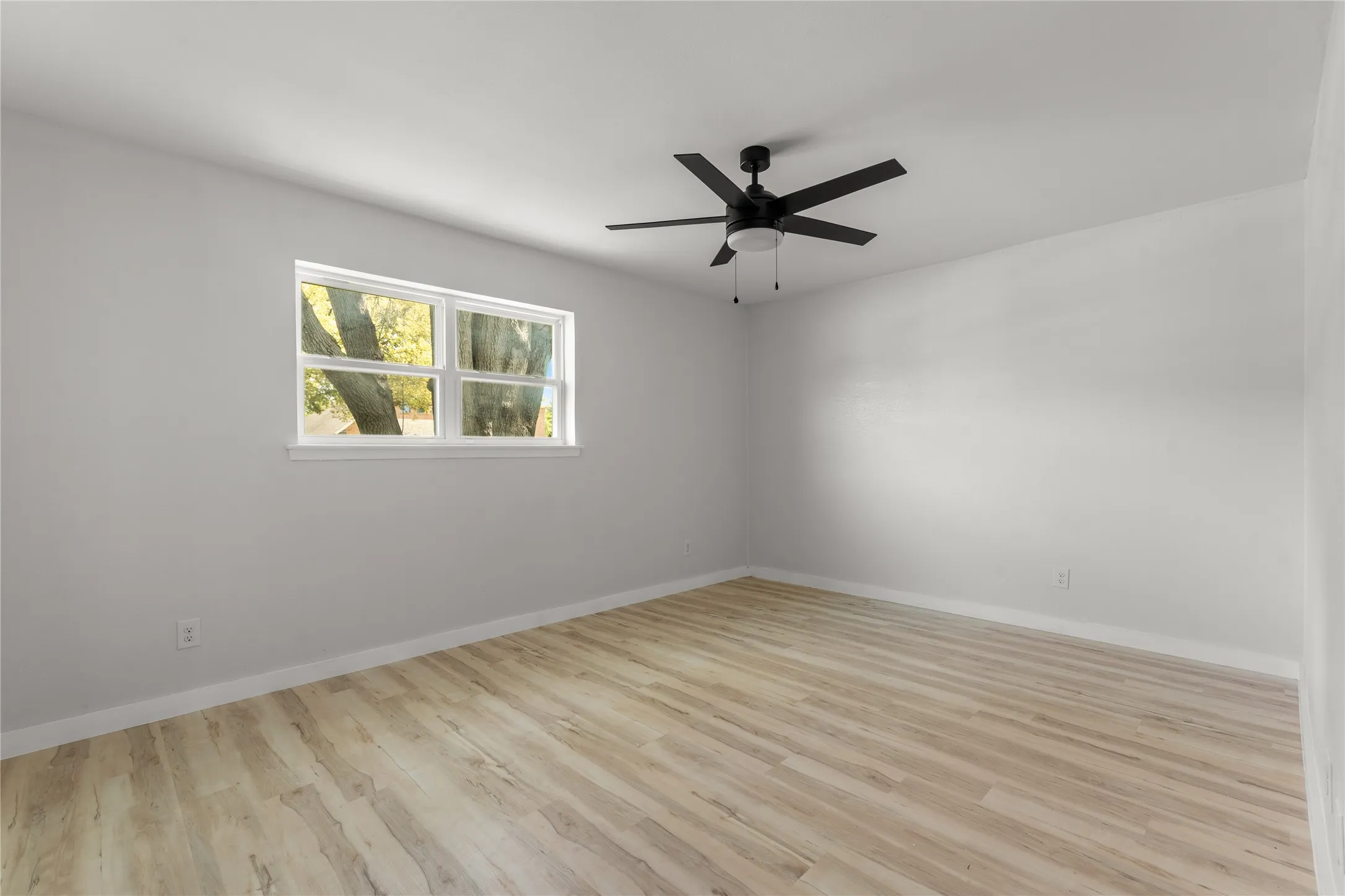 Neutral wall paint, wood-finish flooring, white trim, and a black ceiling fan with integrated lighting