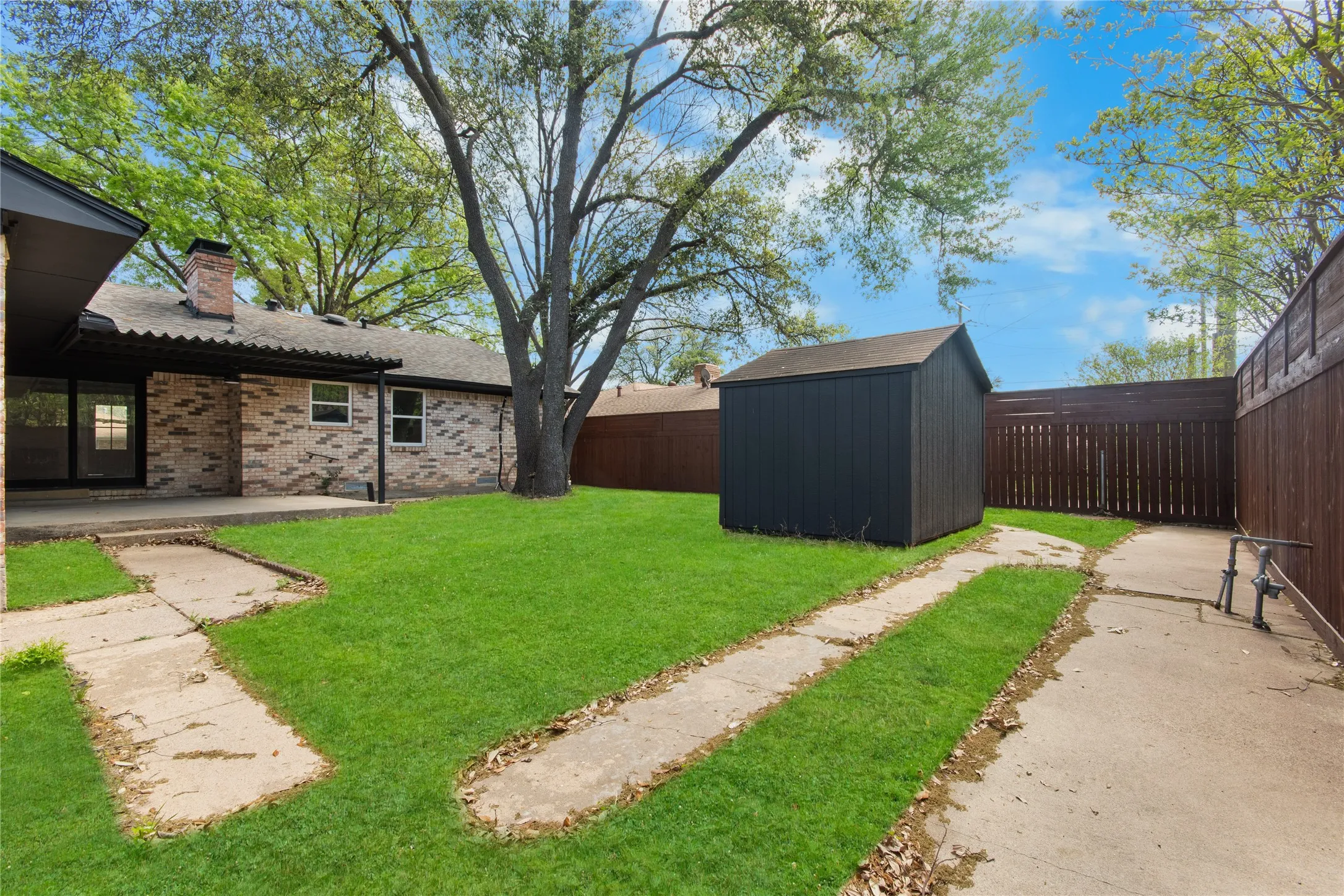Expansive grassy yard with mature trees, a detached storage shed, and durable wood fencing