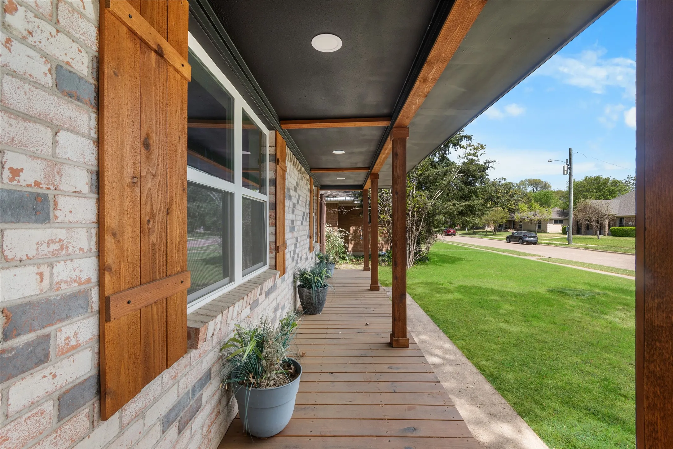 Brick exterior with wood shutters, covered porch with recessed lighting, and wood-finish decking