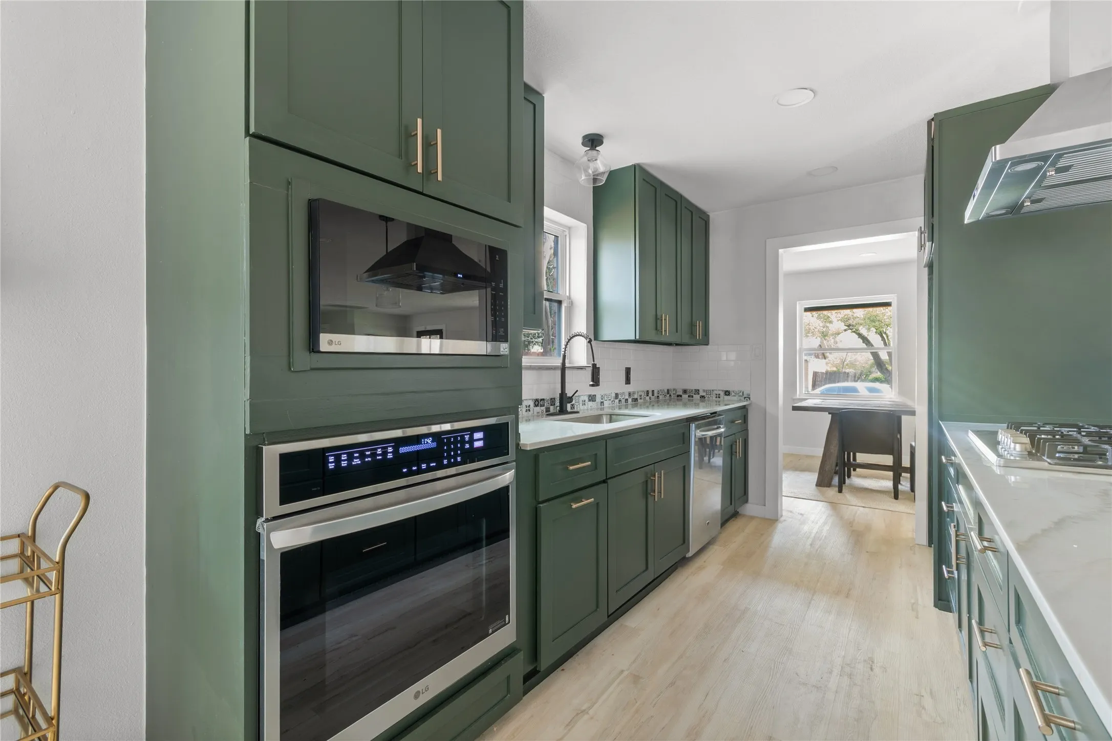 Contemporary kitchen featuring green cabinetry, stainless steel appliances, a tile backsplash, and light-toned flooring