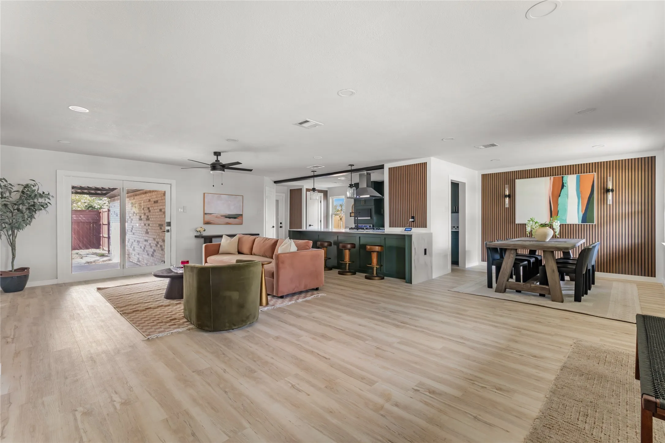 Expansive open-concept living area featuring wood-finish flooring, a contemporary ceiling fan, and sliding glass doors