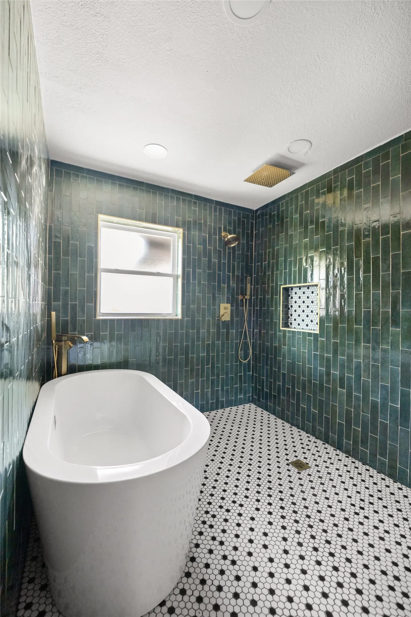 Freestanding soaking tub, green subway tile shower surround, black and white hexagonal tile flooring, and gold-finish fixtures
