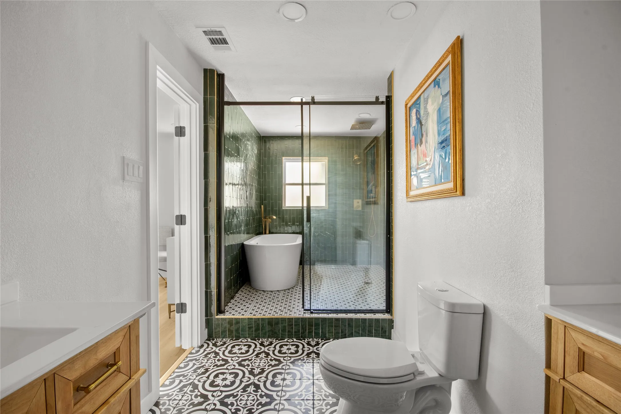 Bathroom featuring a freestanding tub, glass-enclosed shower, patterned floor tile, and wood-finish cabinetry with brass hardware