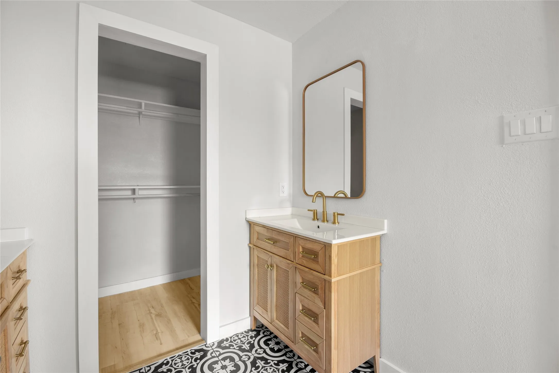 Vanity with a wood-finish cabinet and white countertop, framed mirror with a gold-tone finish, and black and white patterned floor tiles
