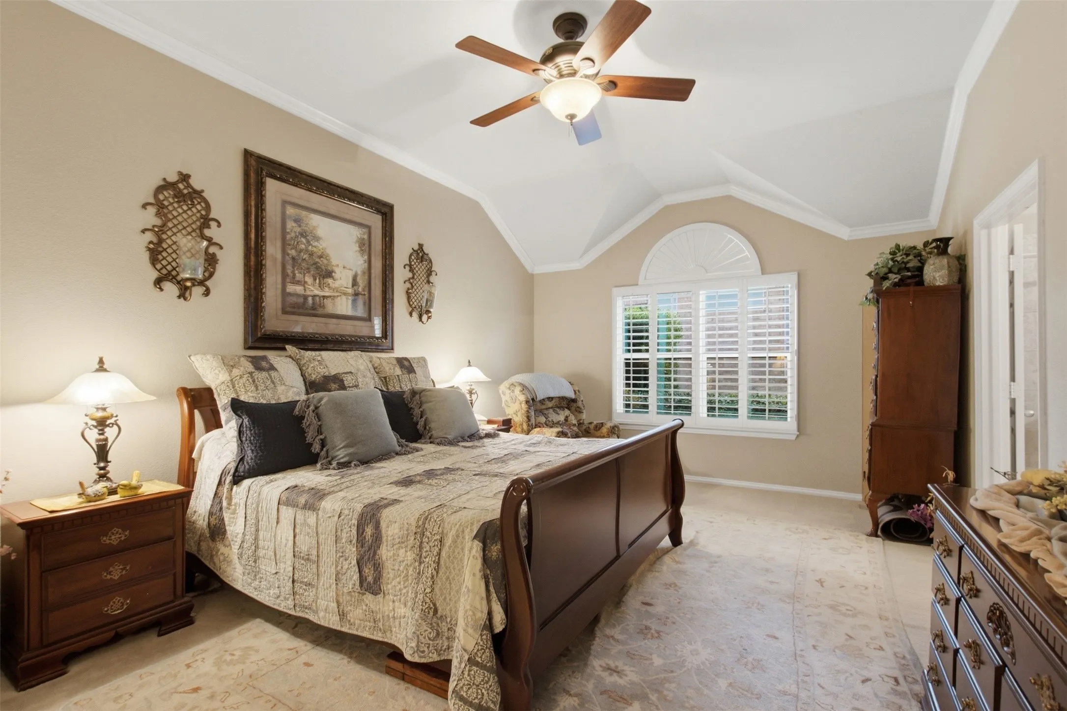 Tray ceiling with crown molding, ceiling fan, arched window with plantation shutters, and light-toned tile flooring