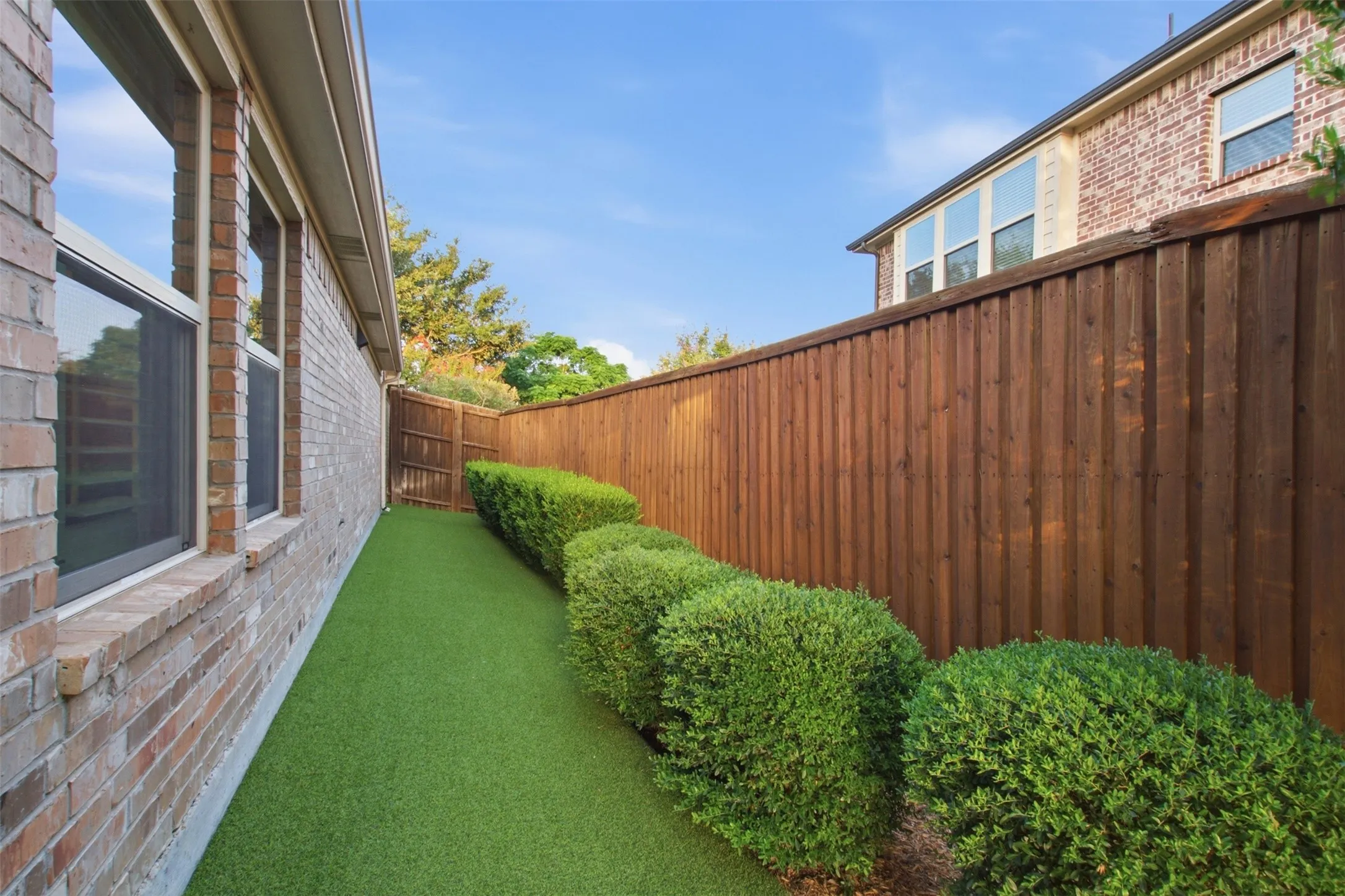 Fenced side yard featuring artificial turf and manicured shrubbery