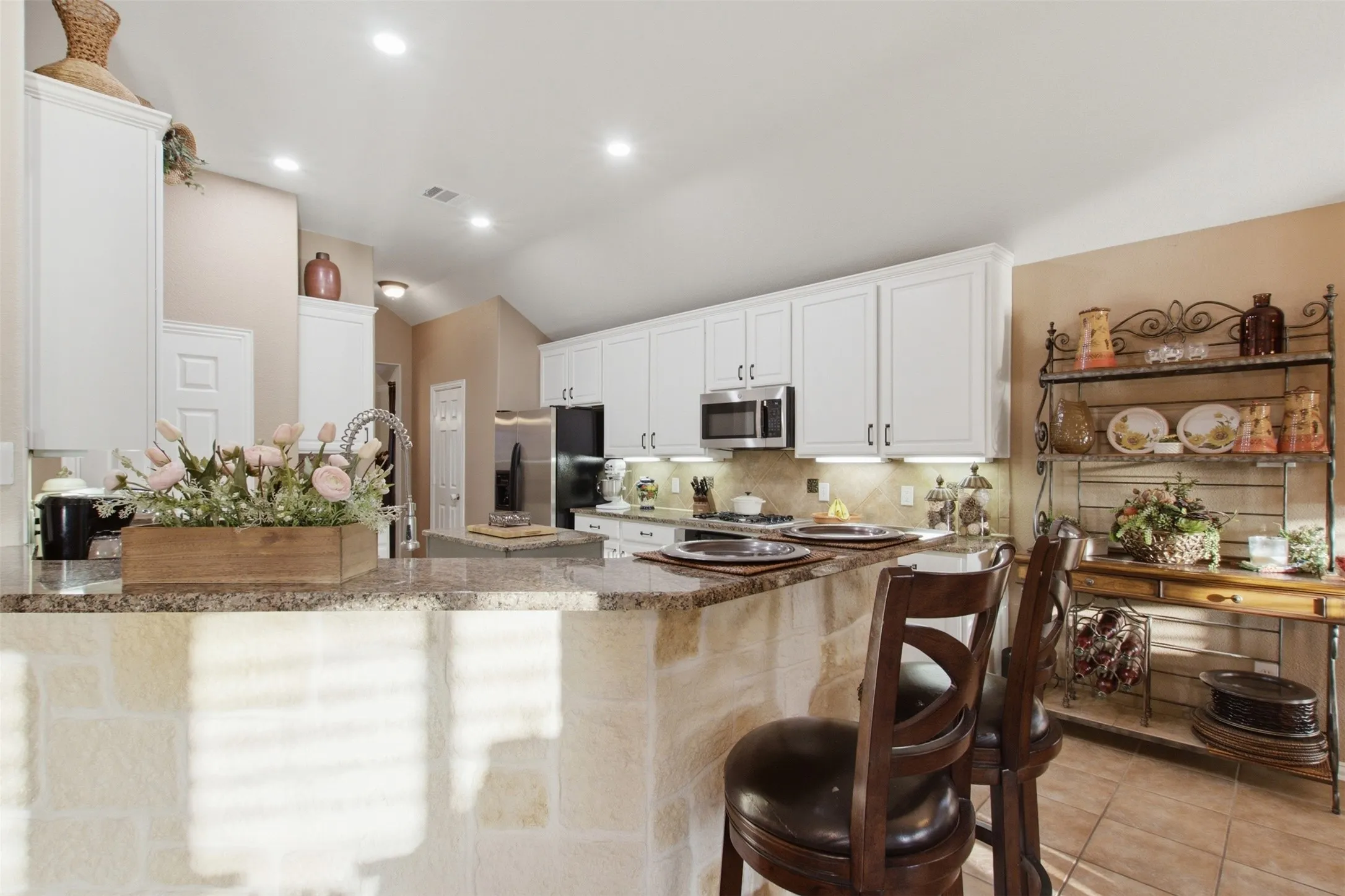 Kitchen featuring white cabinetry, granite countertops, stainless steel appliances, and a stone-clad breakfast bar with seating