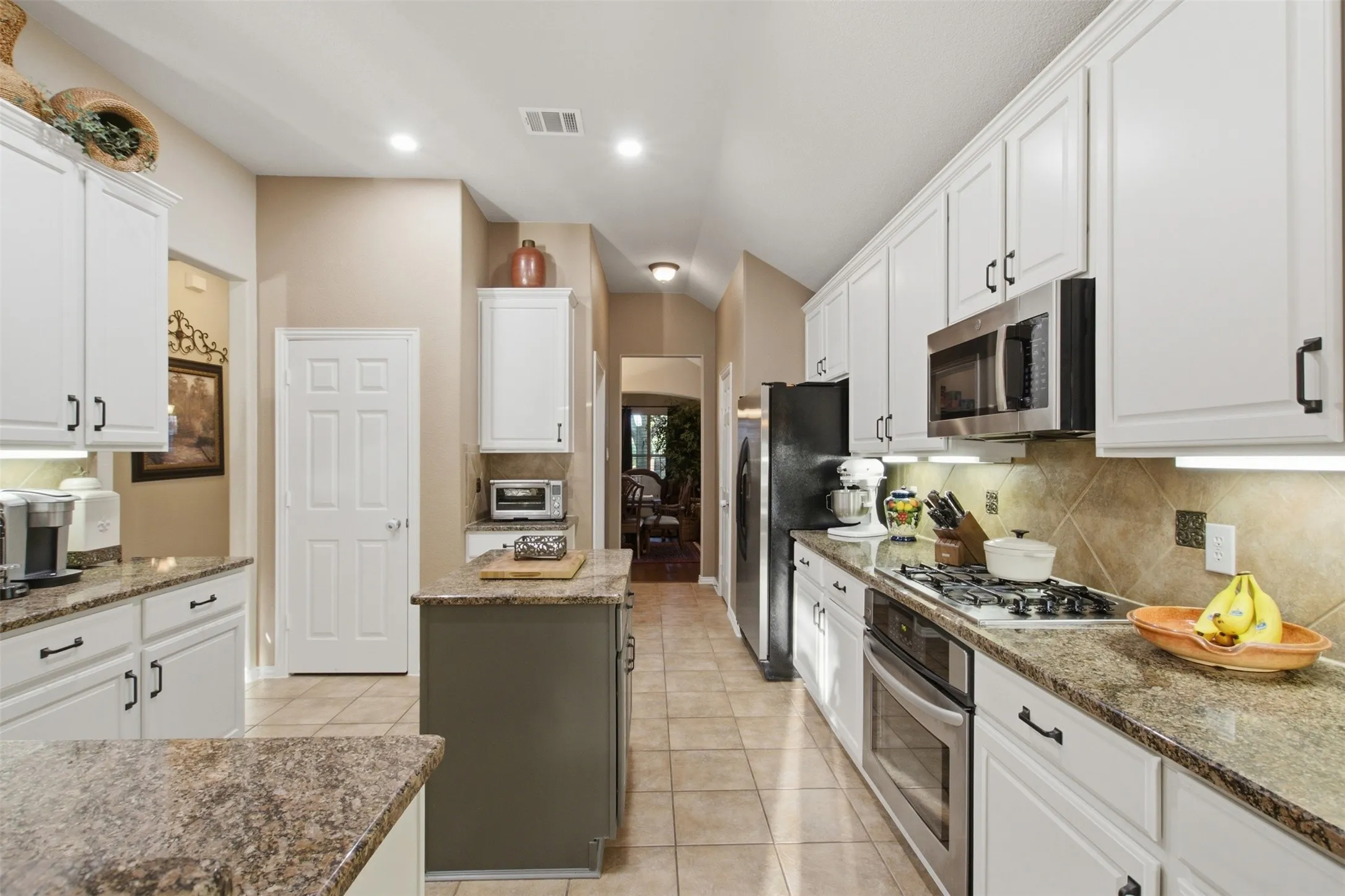 Galley kitchen featuring white cabinetry, stone countertops, stainless steel appliances, tiled flooring, and an island with additional counter space
