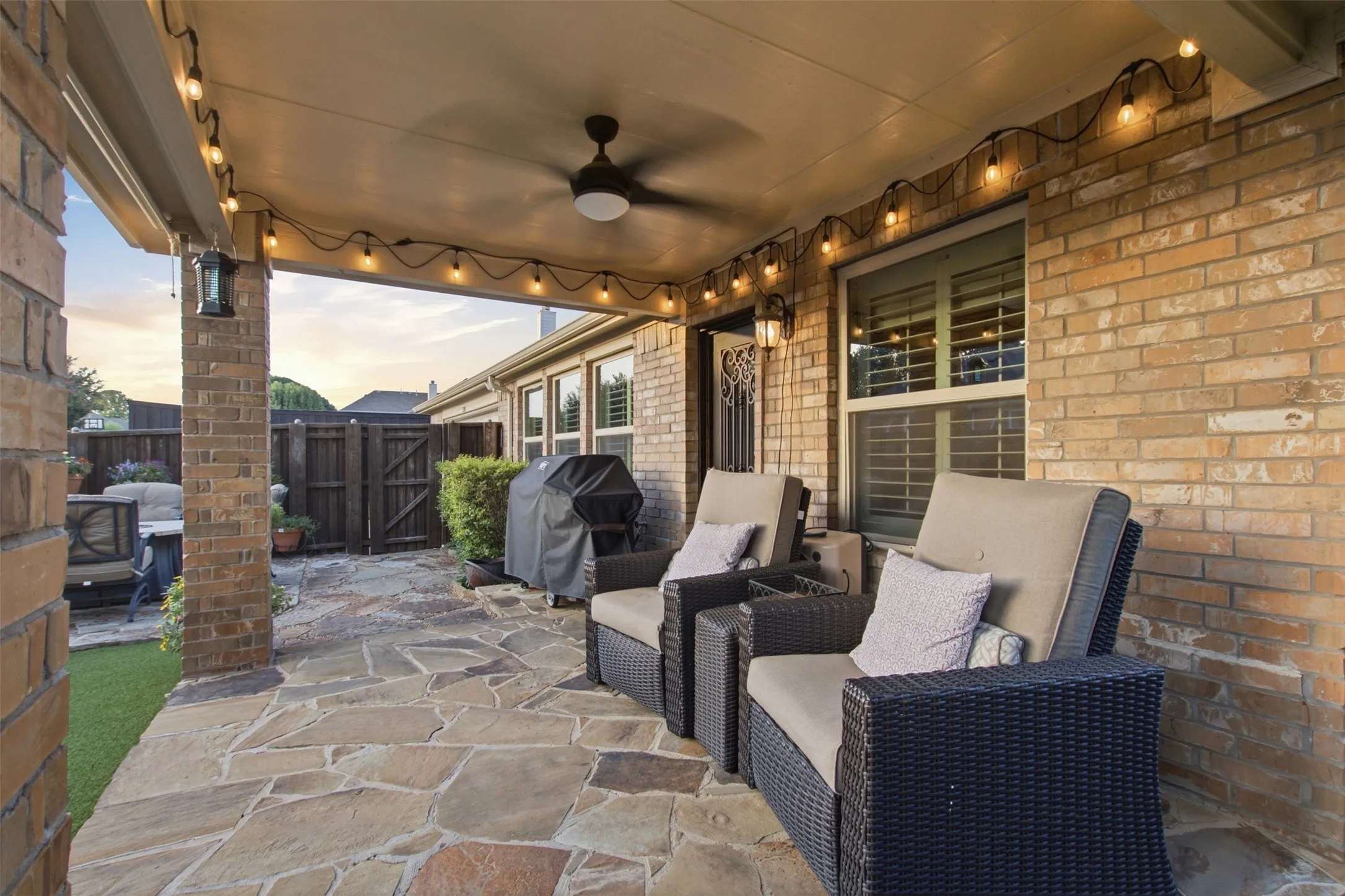 Covered patio with flagstone flooring, brick pillars, a ceiling fan, and string lighting