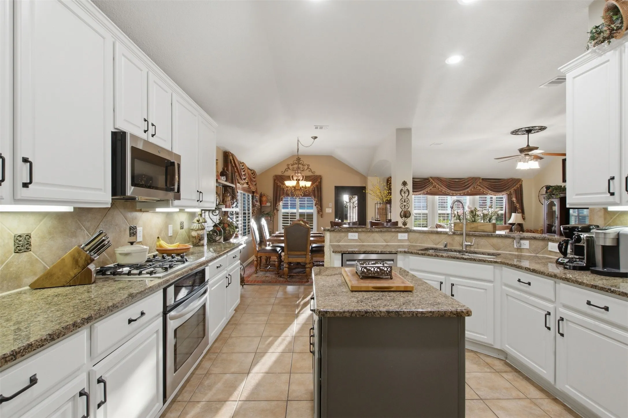 Kitchen with white cabinetry, stone countertops, stainless steel appliances, and a central island