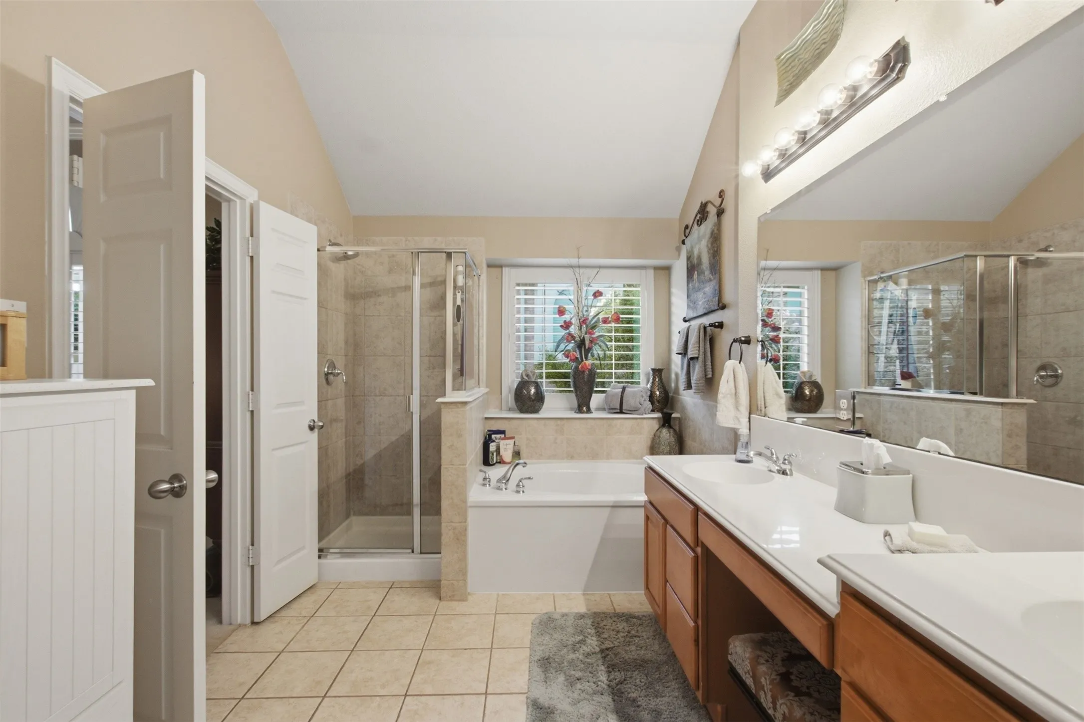 Double vanity with integrated sinks, framed mirror, built-in soaking tub, tile flooring, and a glass-enclosed shower