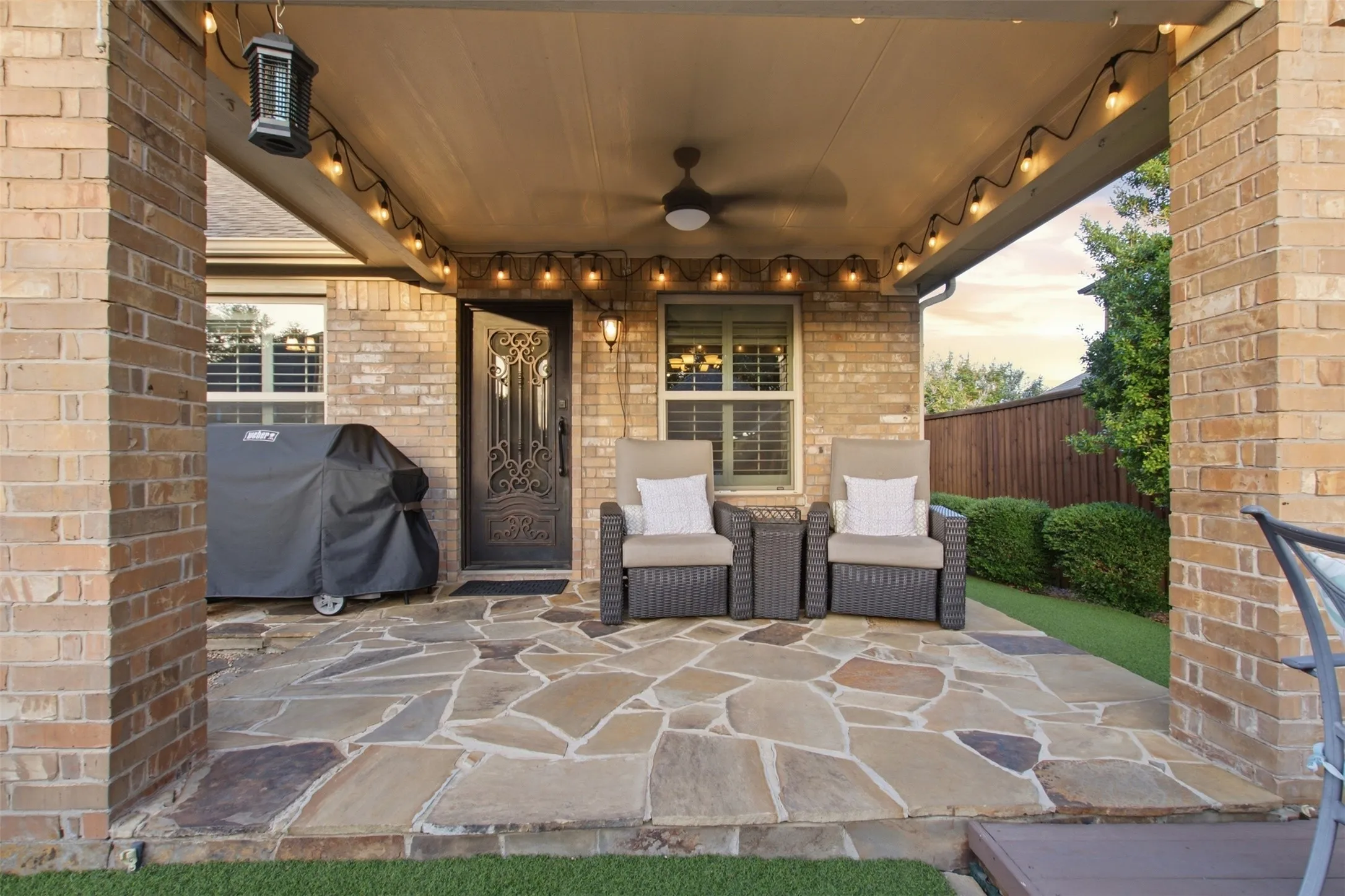 Covered patio with flagstone flooring, brick columns, ceiling fan, and decorative wrought iron entry door