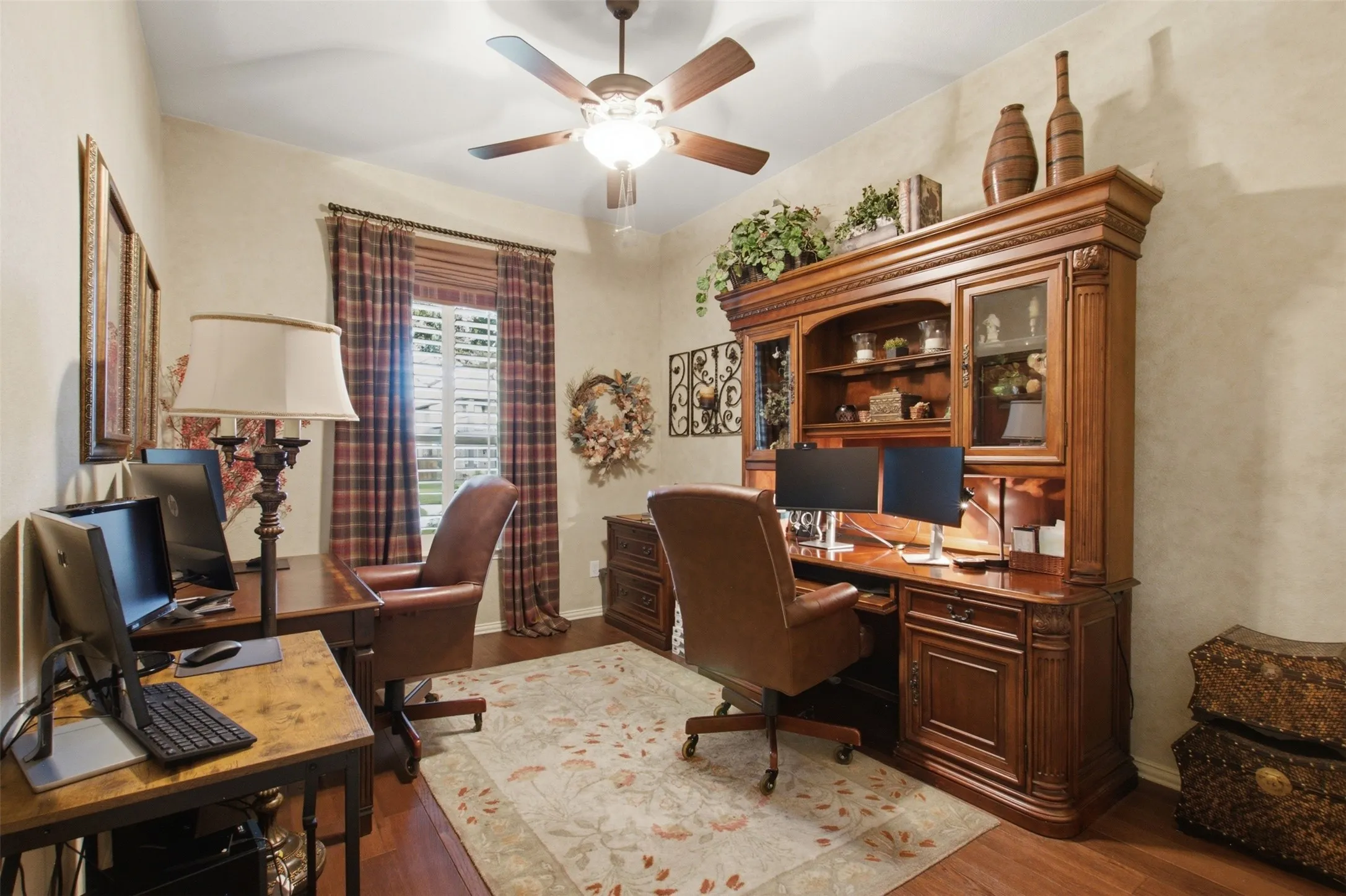 Wood-finish flooring, ceiling fan with integrated lighting, window with plantation shutters, and a built-in wooden hutch with glass-front cabinetry