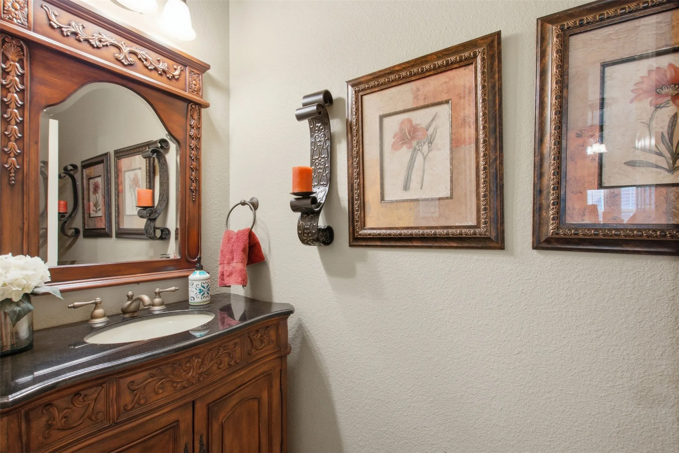 Carved wood-finish vanity with an undermount sink, dark stone countertop, and ornate wood-framed mirror