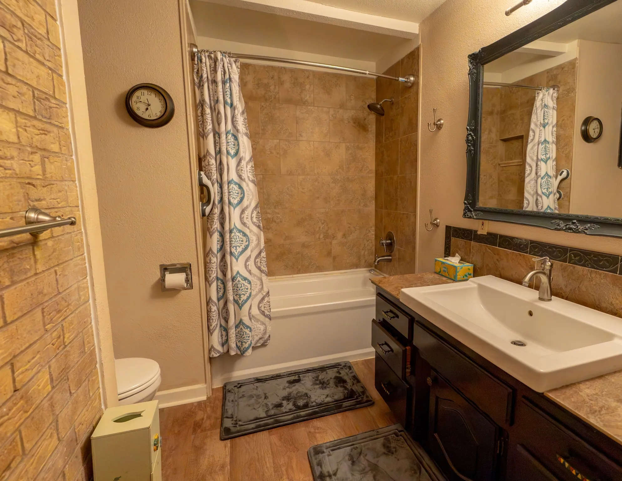 Bathroom with a tiled shower-over-tub, dark wood-finish vanity with an integrated sink, and wood-finish flooring