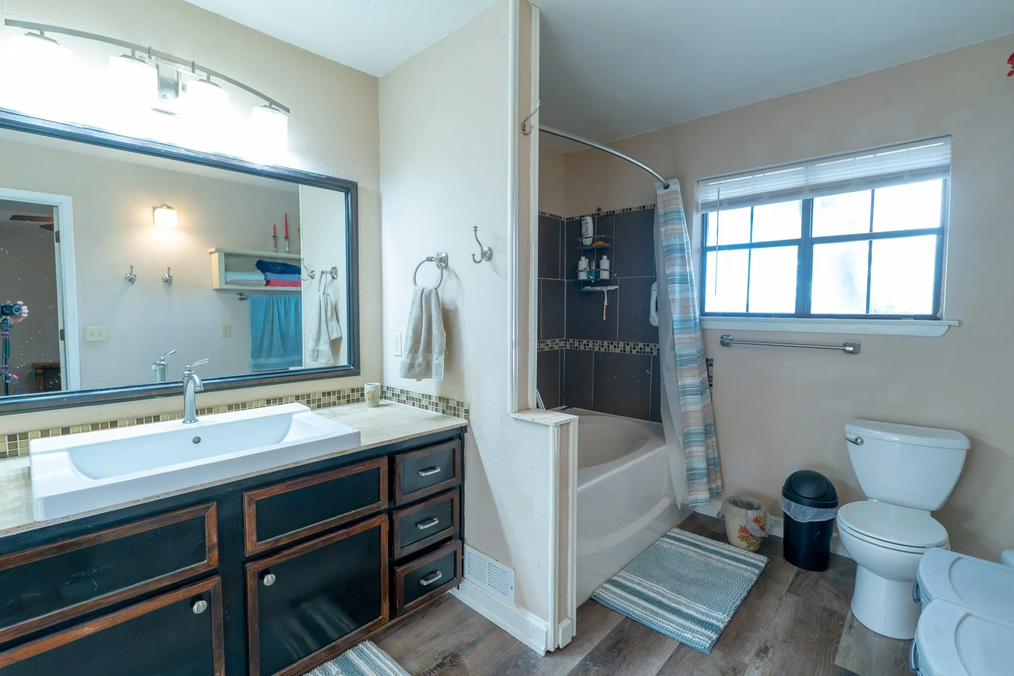 Wood-finish flooring with a vanity featuring a vessel sink and a tiled backsplash