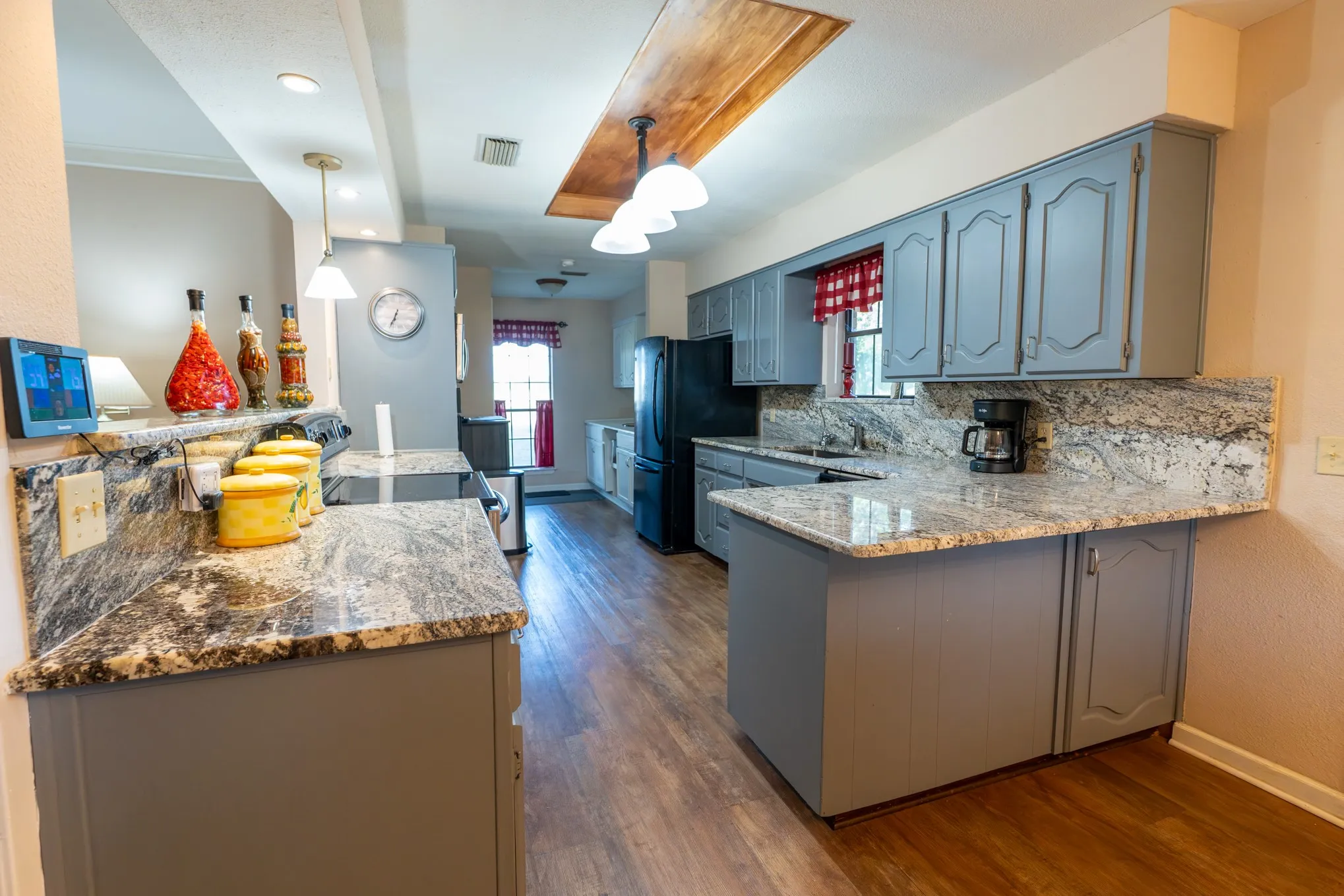 Light gray cabinetry, granite countertops, wood-finish flooring, recessed lighting, and a wood-panel ceiling accent