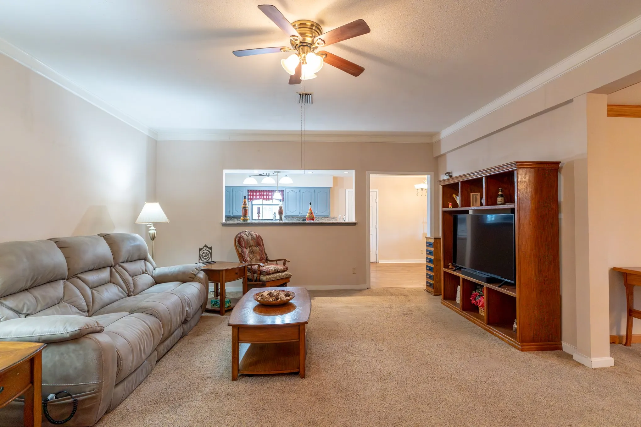 Recessed pass-through opening to the kitchen, crown molding, and a ceiling fan with integrated lighting