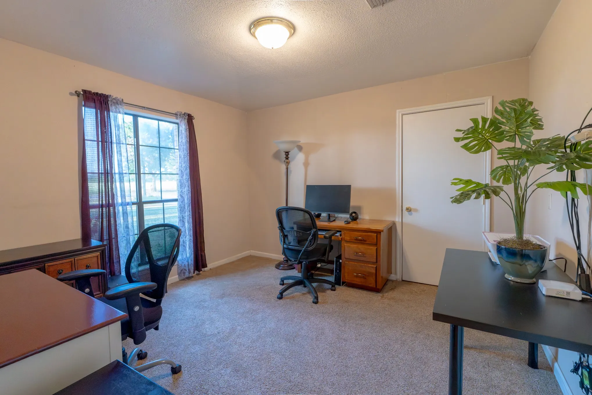 Carpeted room with a ceiling-mounted light fixture, window with drapery, and a white interior door
