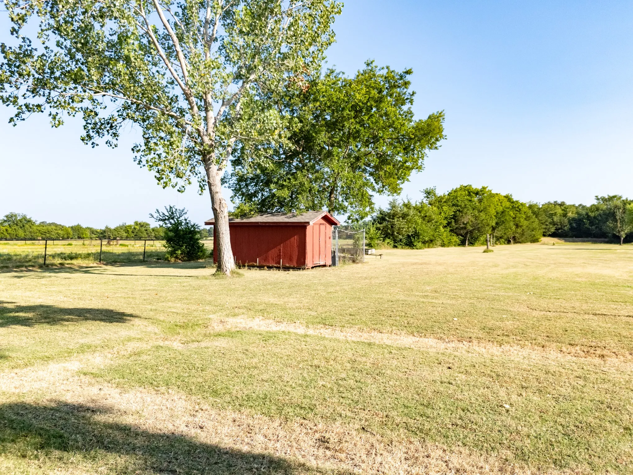 Expansive grounds featuring a red shed, mature trees, and perimeter fencing