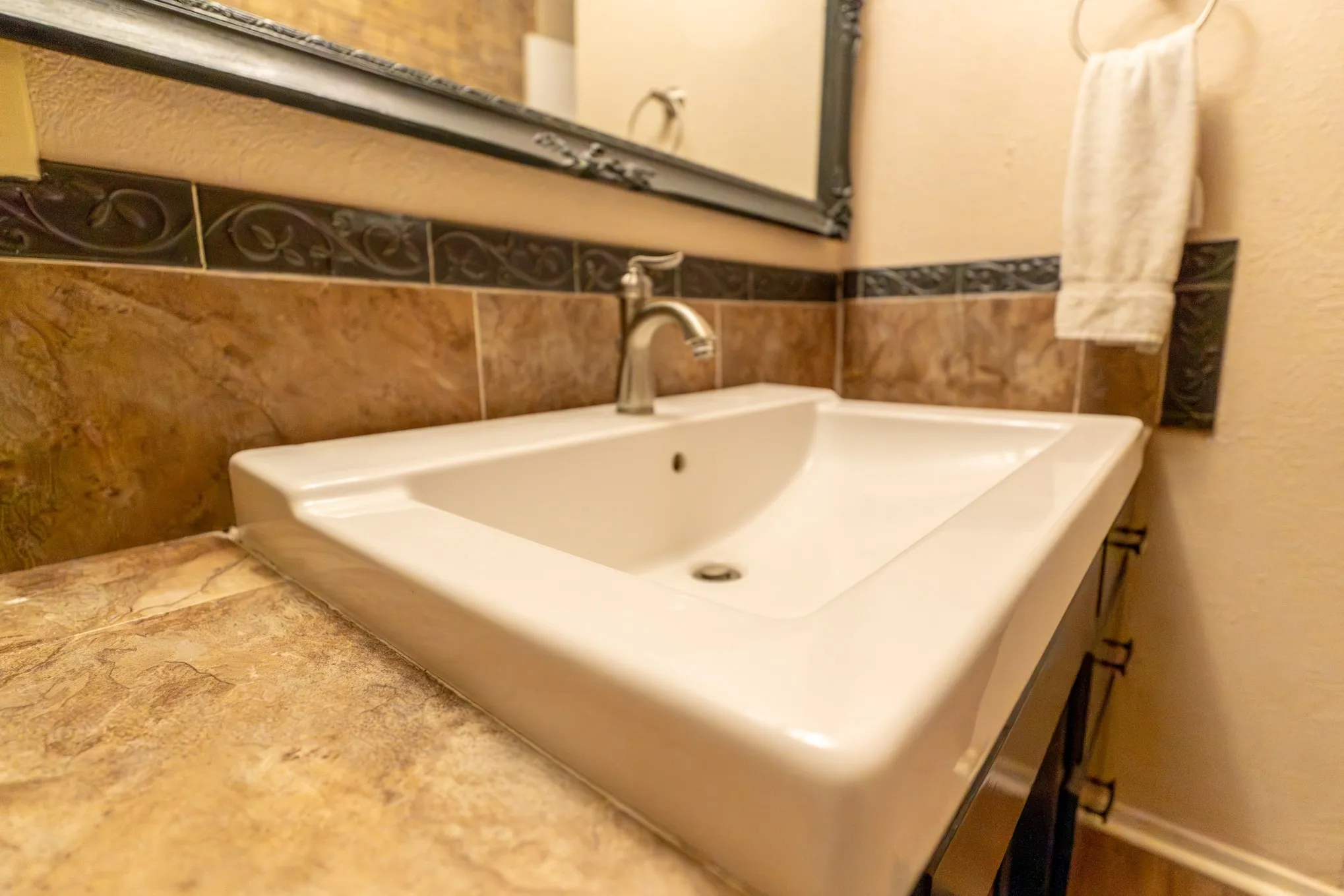 White ceramic basin sink with a single-handle faucet, set into a vanity with a patterned tile backsplash and decorative accent tiles