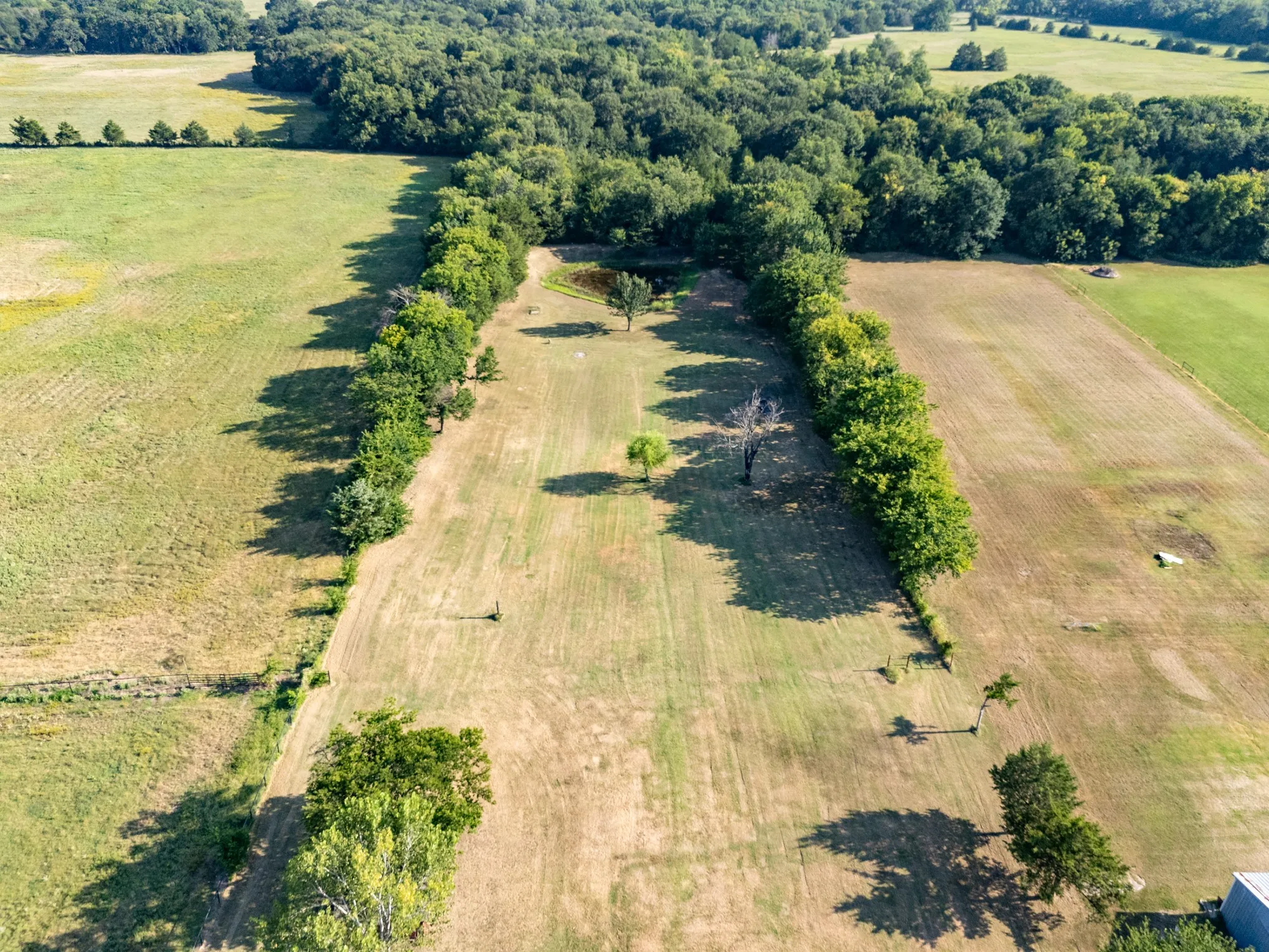 Expansive land featuring a natural pond, established tree lines, and surrounding fields
